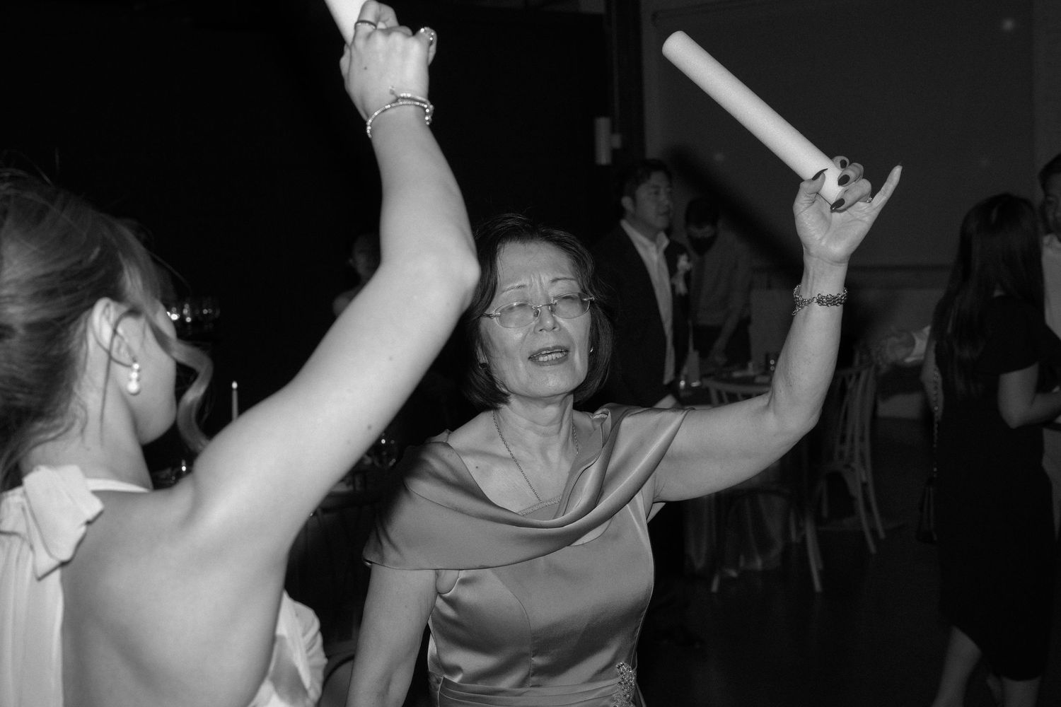 Woman dances joyfully with arms raised at black and white wedding party.