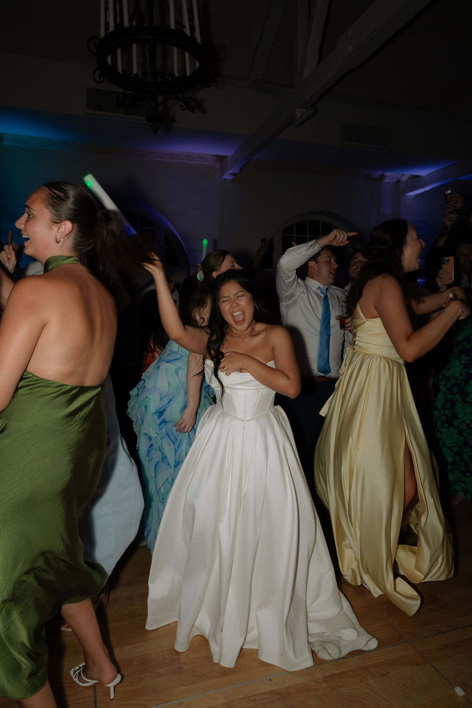 Joyful bride in white ball gown dancing energetically with guests on the wedding reception dance floor.