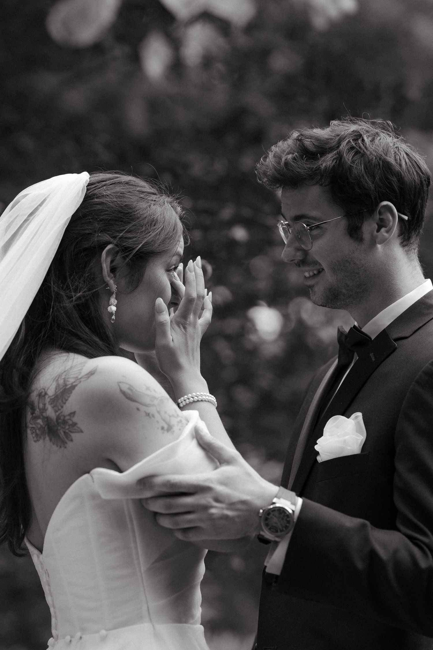Black and white photo of emotional bride crying while groom smiles tenderly during outdoor wedding ceremony.