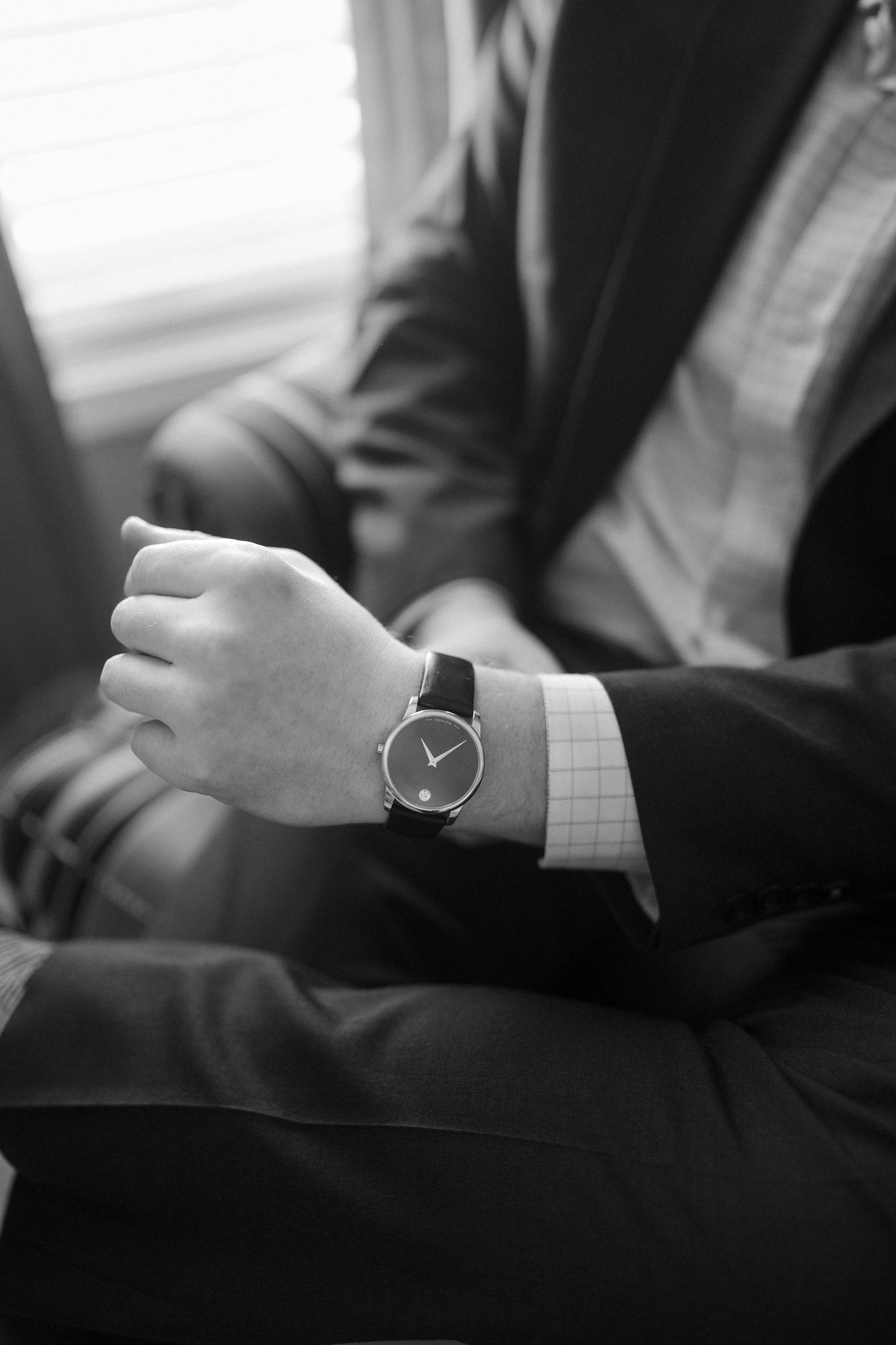 Close-up of a man in a suit checking a minimalist black dial wristwatch, black and white photo.