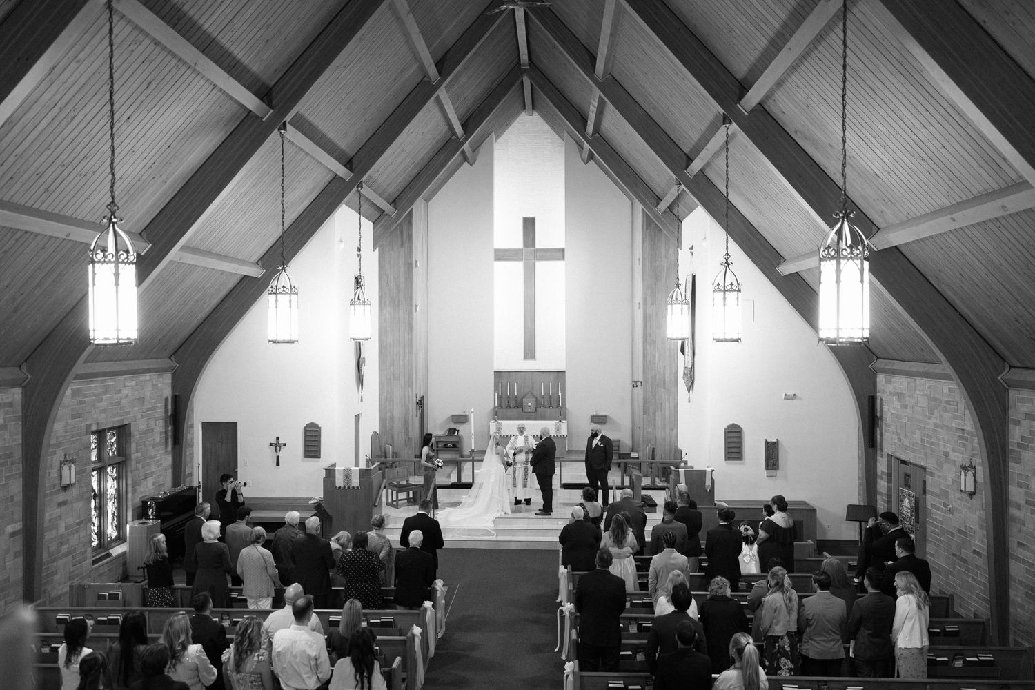 Black and white photo of a wedding ceremony inside a traditional church with wooden beams and a large cross.