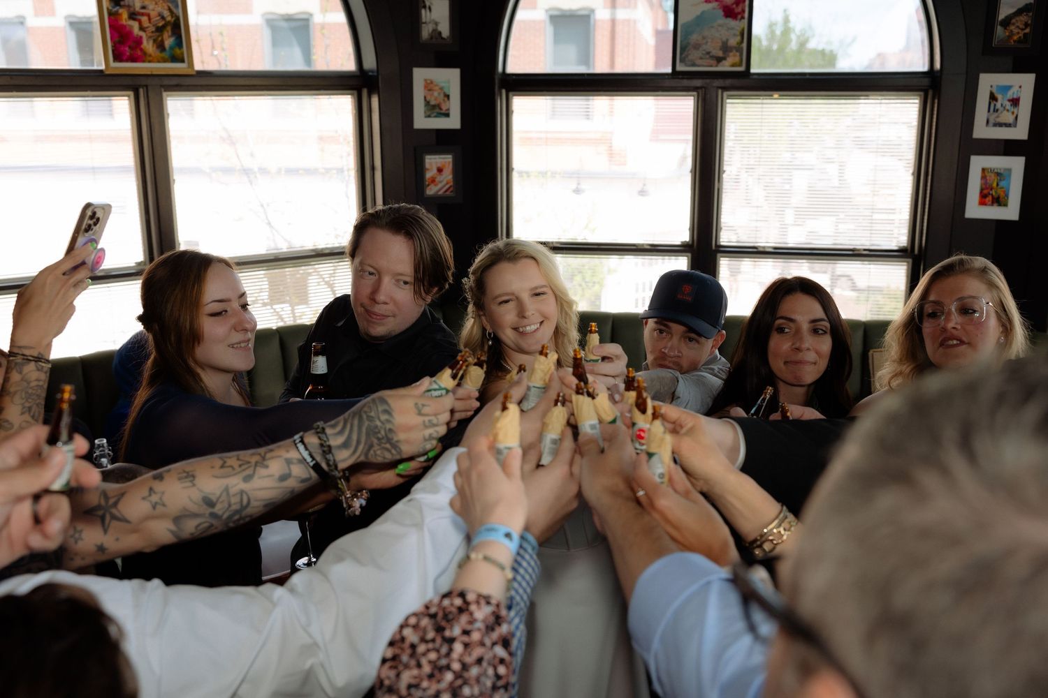 Group of friends toasting drinks together at a lively restaurant gathering, smiling and celebrating indoors.