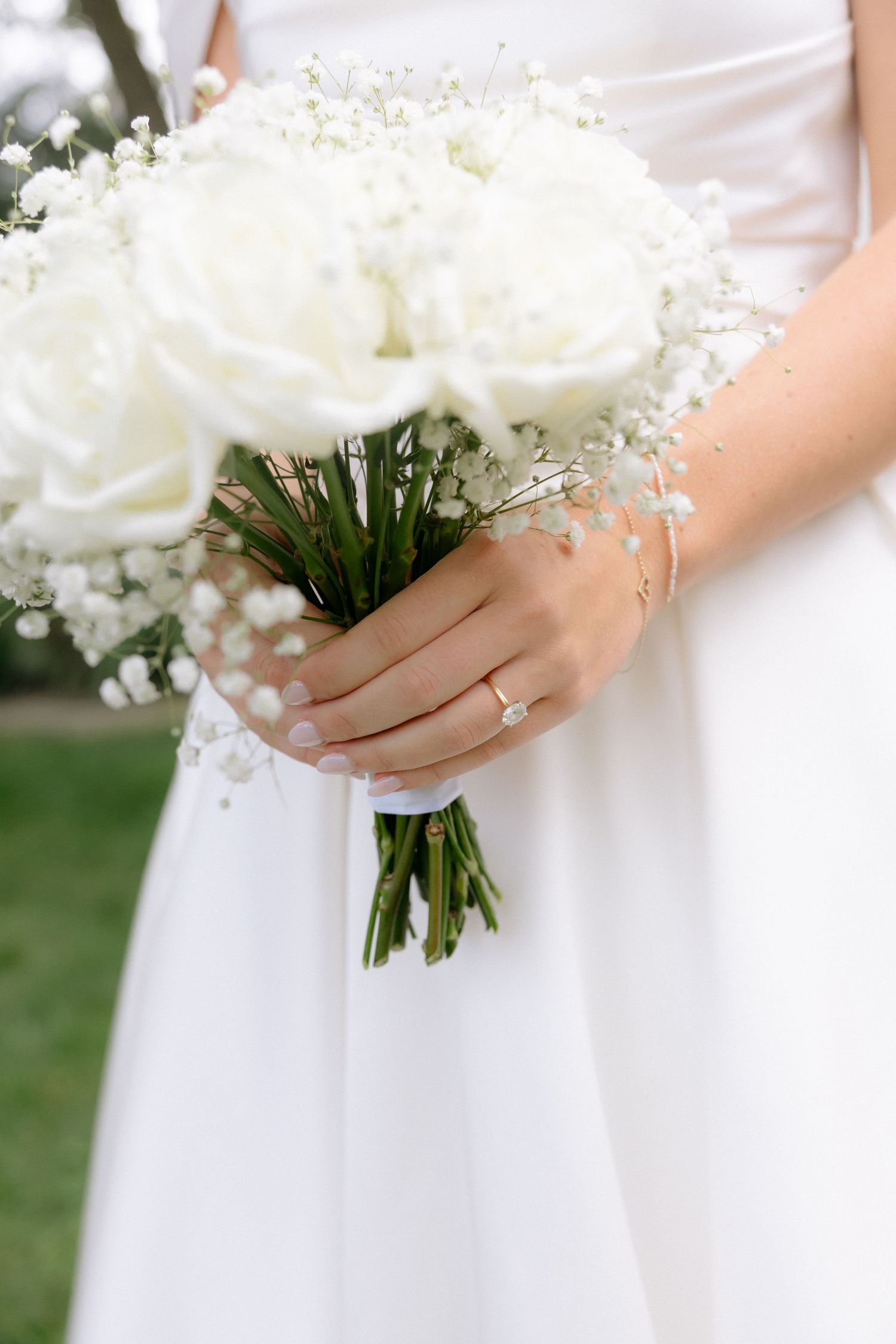 Bride holding white rose and baby's breath wedding bouquet with diamond ring and bracelet visible.