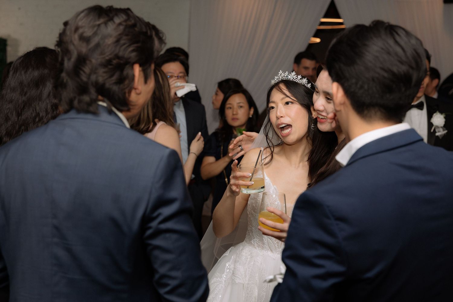 Bride wearing tiara mingles with wedding guests at reception party.