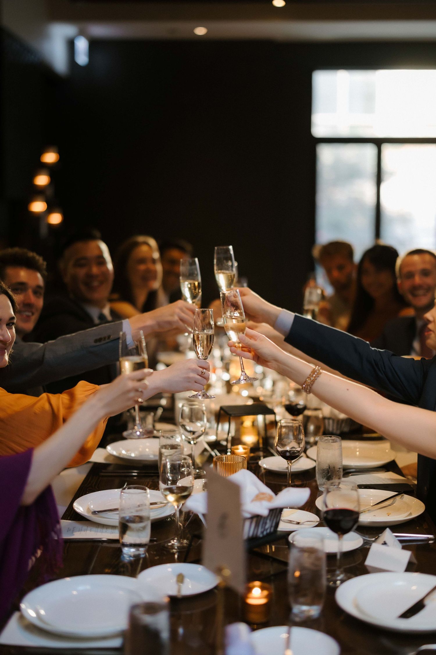 Diverse group of elegantly dressed guests raising champagne glasses in a toast at a formal dinner party.