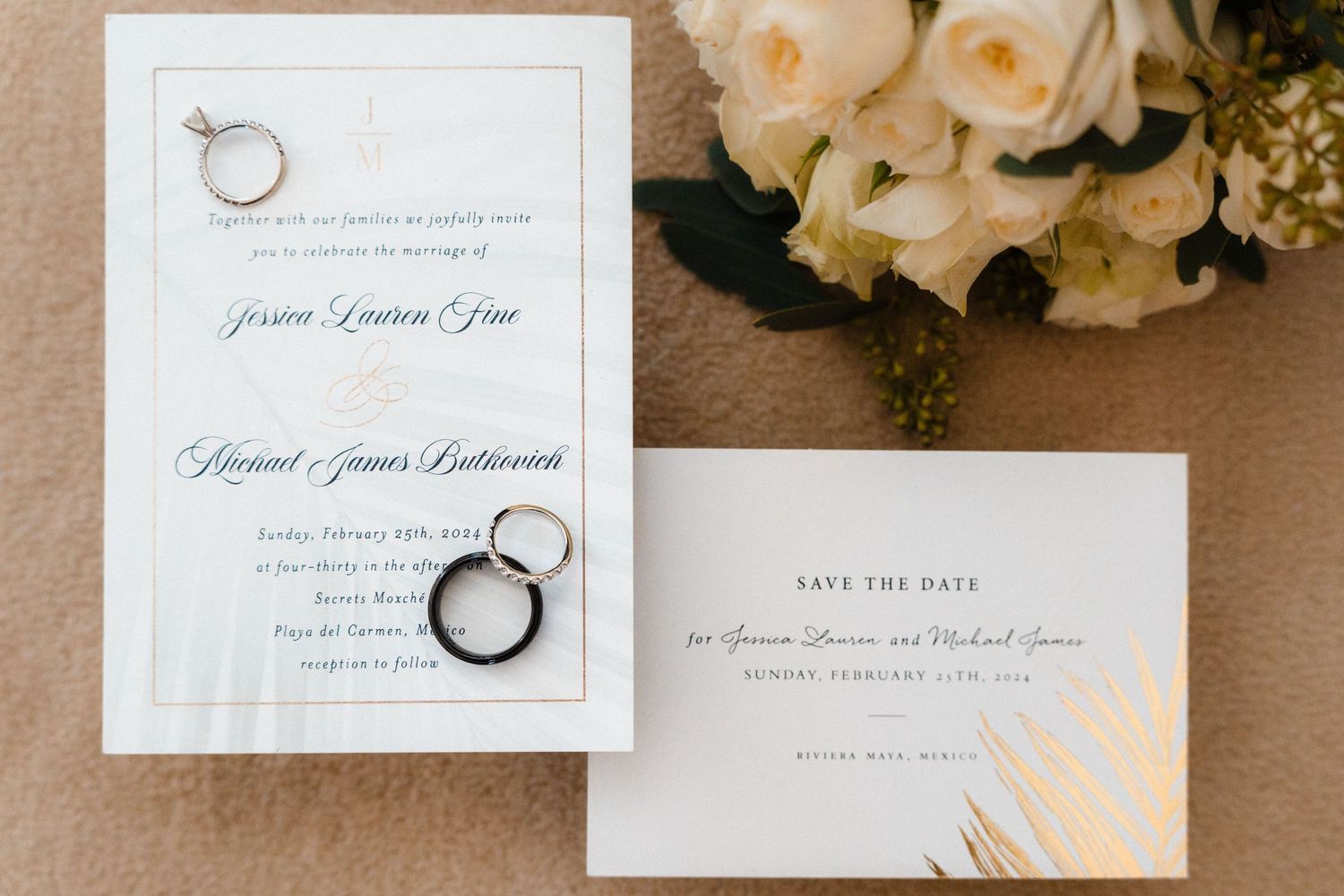Wedding invitation suite with rings and white roses on neutral background.