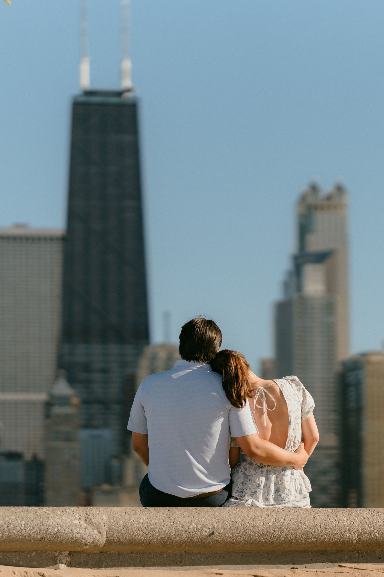 Couple sitting together on lakefront wall gazing at Chicago skyline with John Hancock Tower.