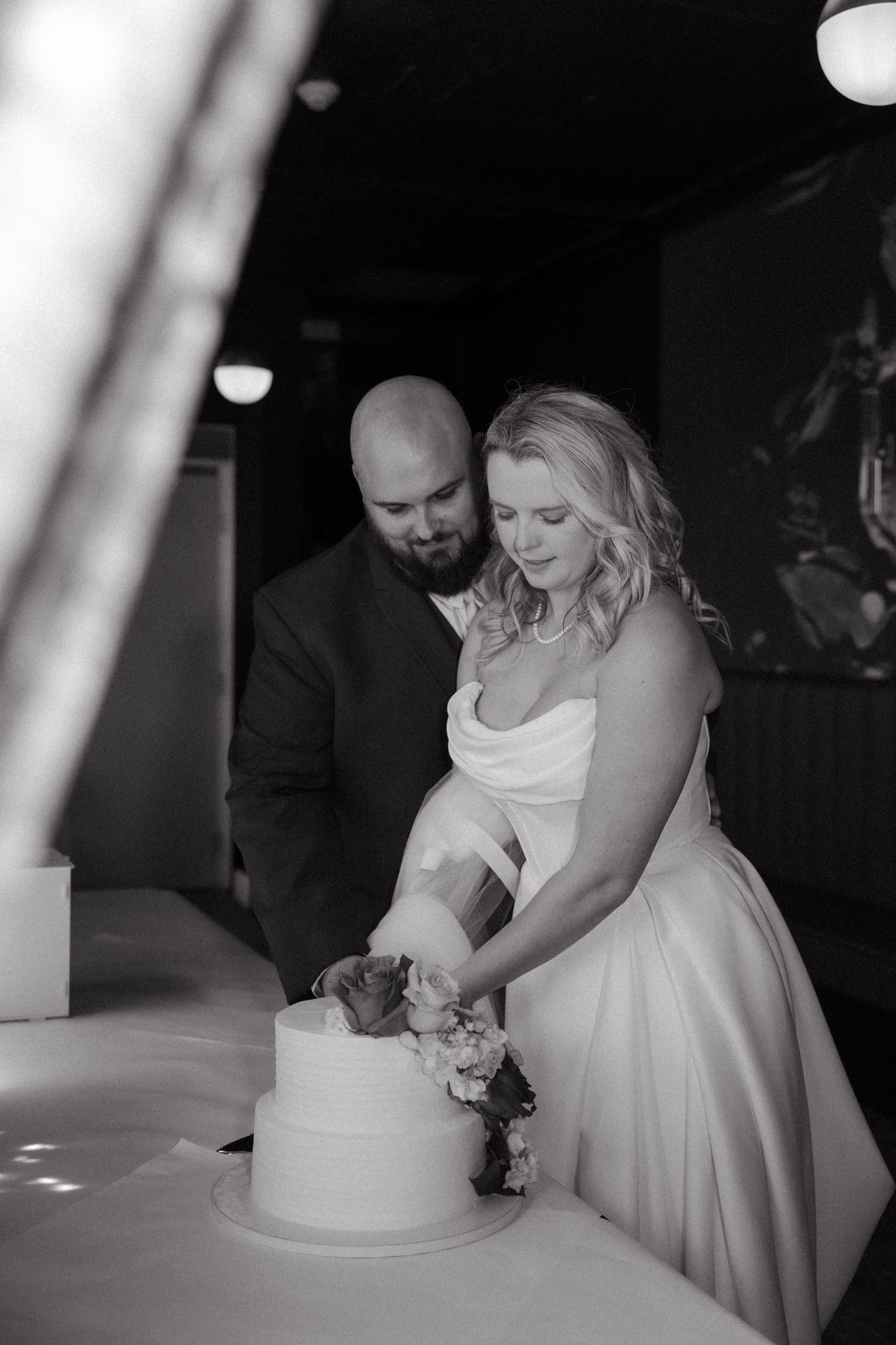 Black and white photo of bride and groom cutting their wedding cake together.