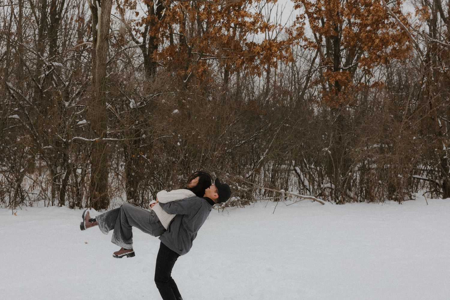 Person performing a high kick in snowy winter landscape with bare trees in background.