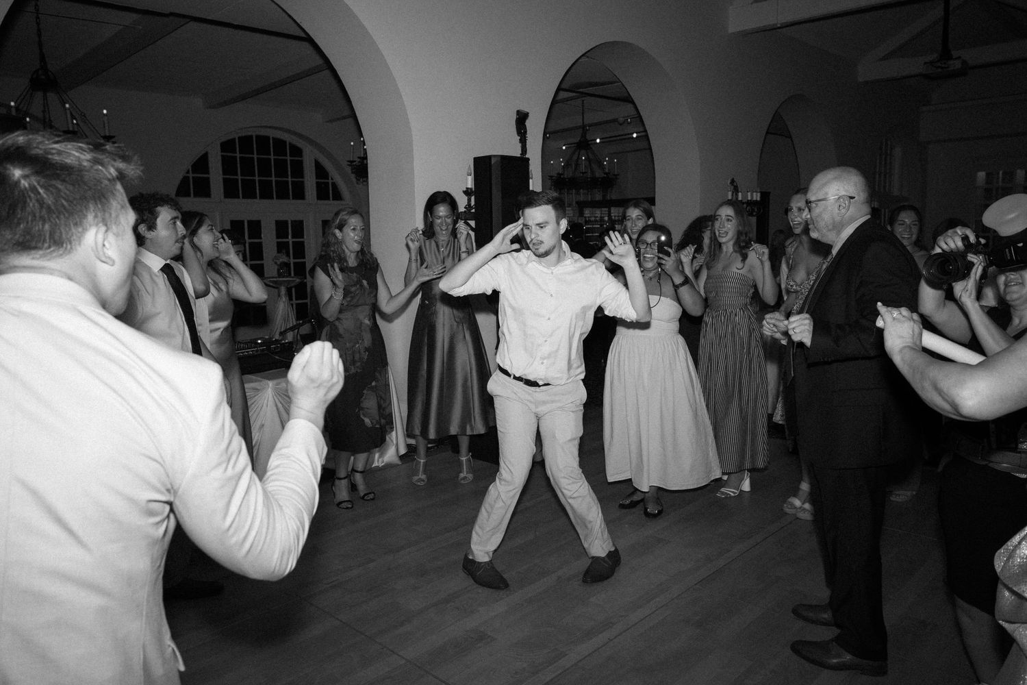 Guest energetically dancing in a circle at a lively black and white wedding reception.