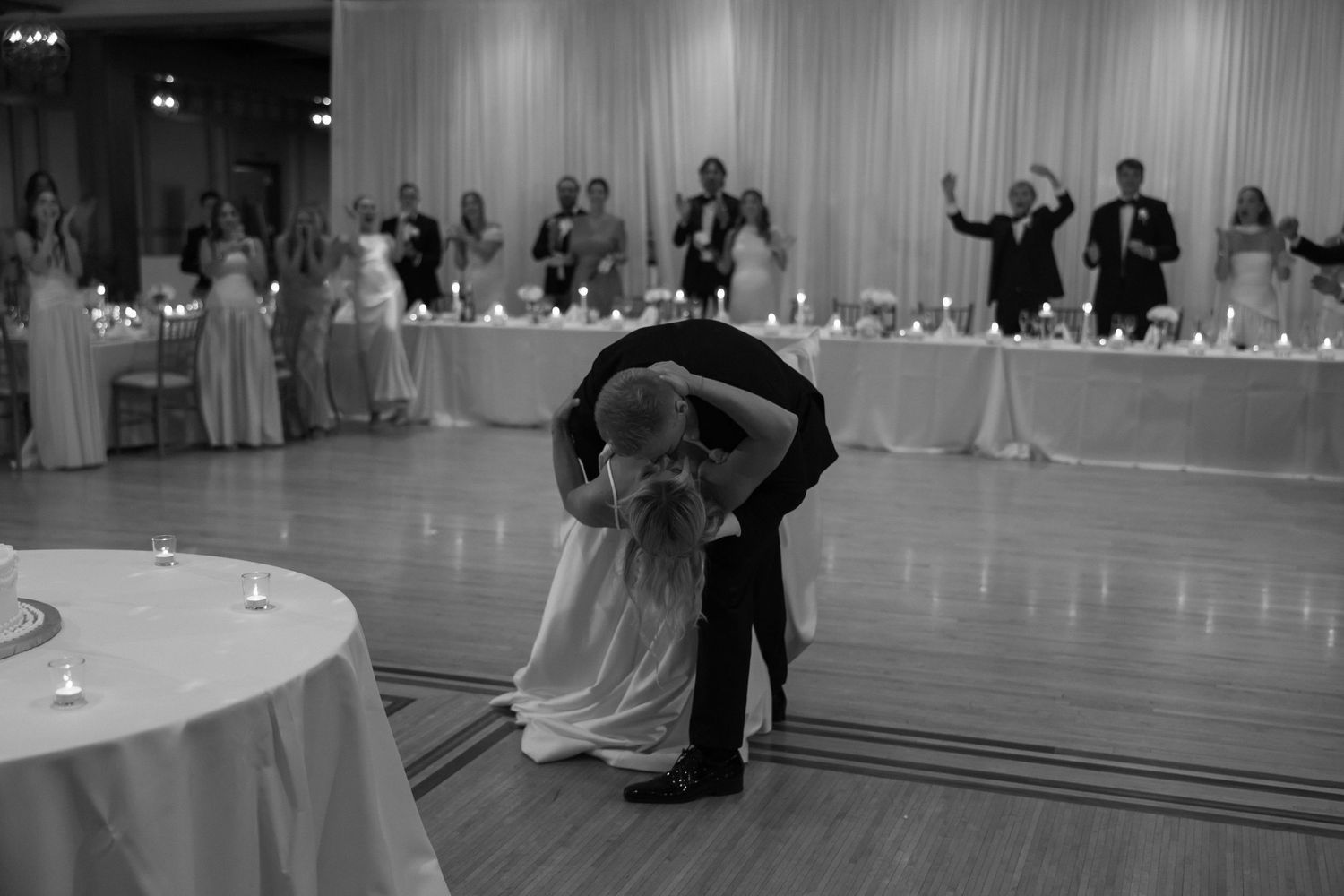 Black and white photo of bride and groom sharing dramatic dip during first dance at reception.