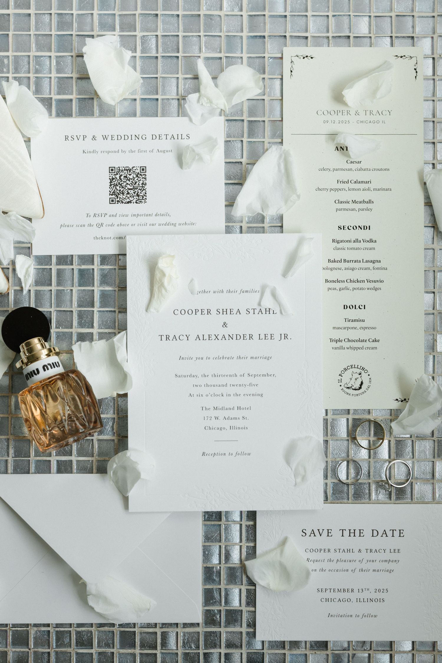 Elegant wedding stationery suite with invitation, menu, save the date, and RSVP card on silver tile with white petals.