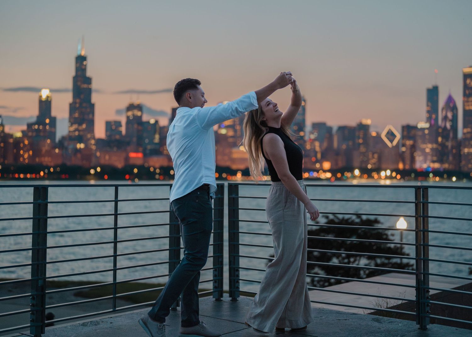 A joyful couple dances together on a waterfront deck with the stunning Chicago city skyline at dusk.