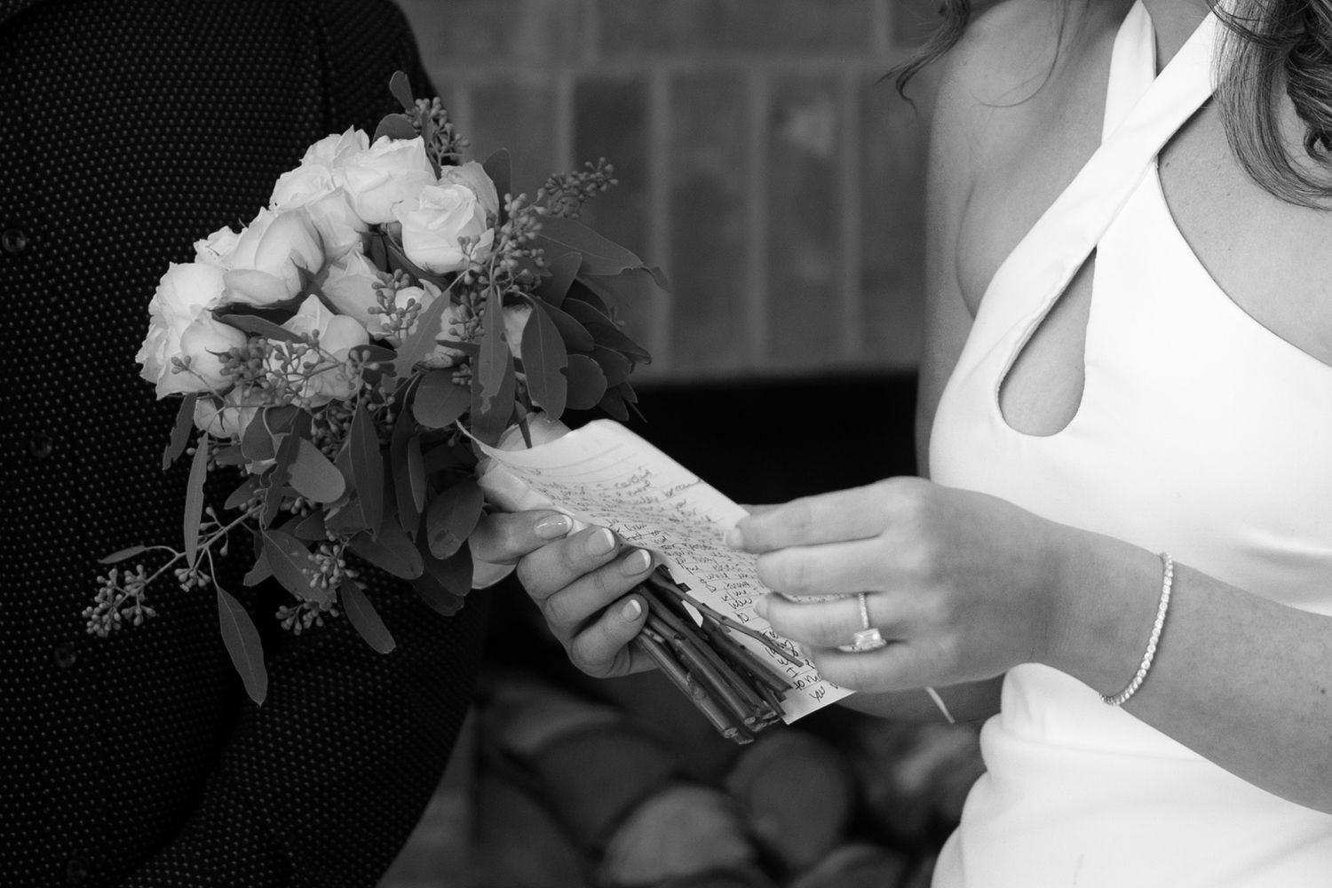 Black and white close-up of bride holding white rose bouquet and vow notes.