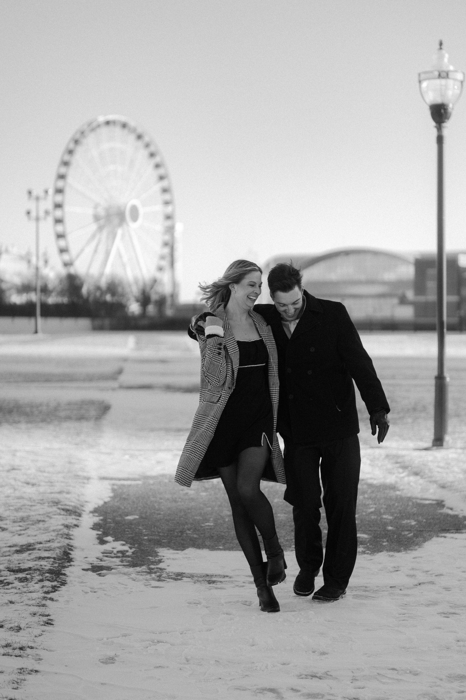 Black and white photo of couple walking in snow near Navy Pier Ferris wheel.