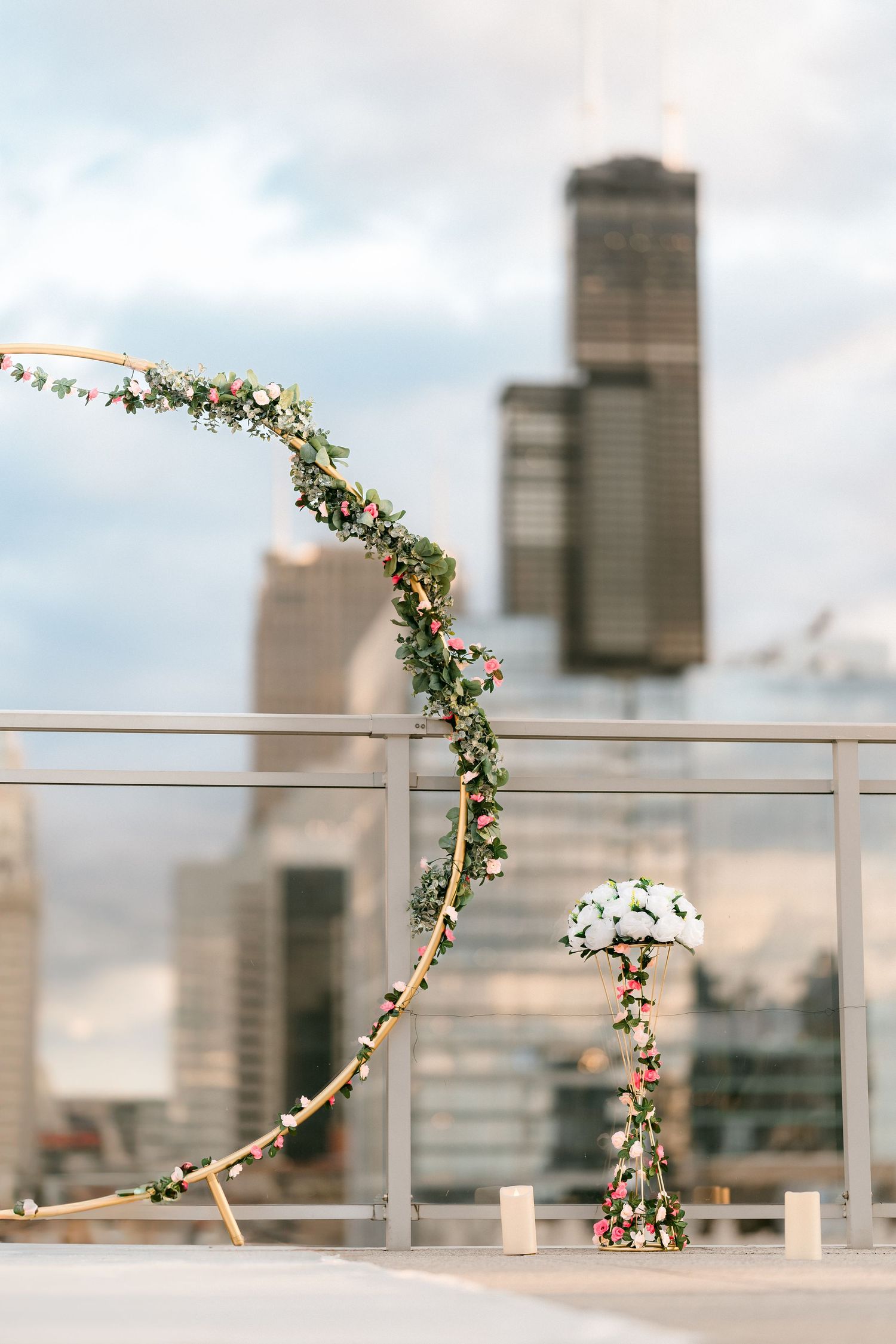 Circular floral hoop arch with greenery and flowers on a rooftop with Chicago Willis Tower skyline.