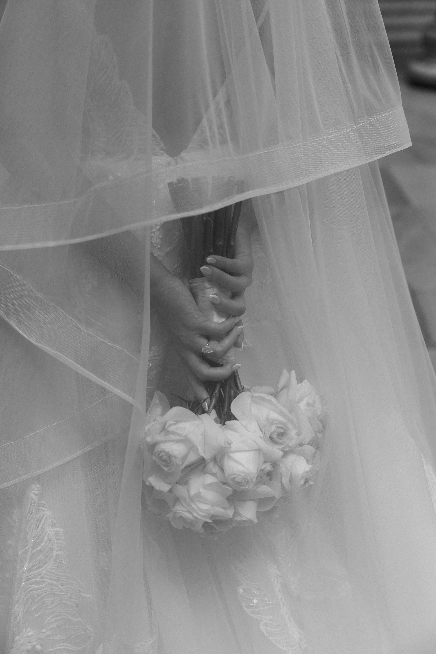 Black and white photo of a bride holding a white rose bouquet beneath her flowing wedding veil.