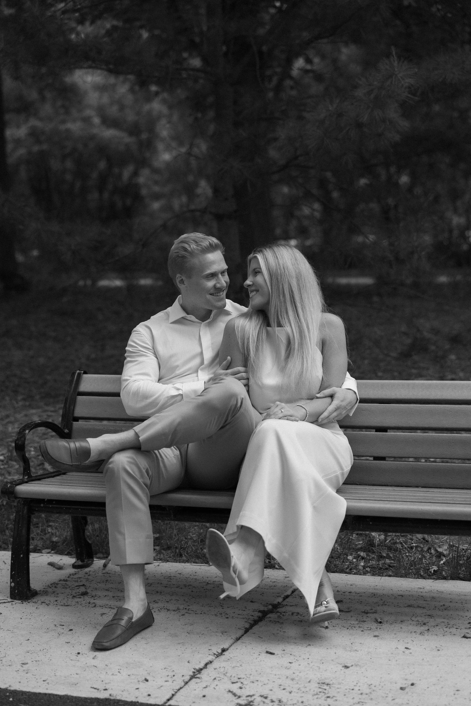 Black and white photo of a smiling couple sitting closely together on a park bench, gazing at each other.