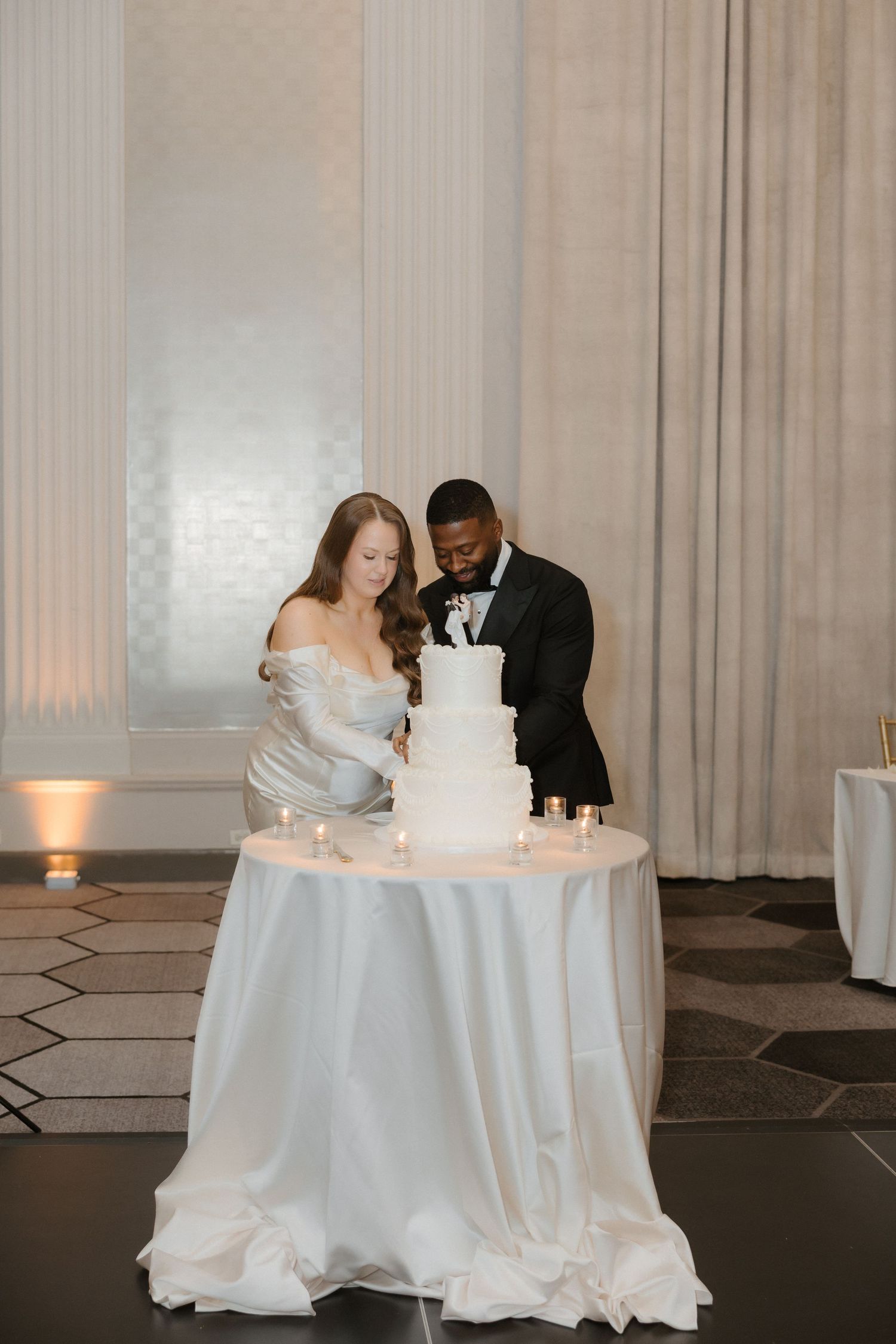 Bride and groom cutting white tiered wedding cake at elegant reception venue.