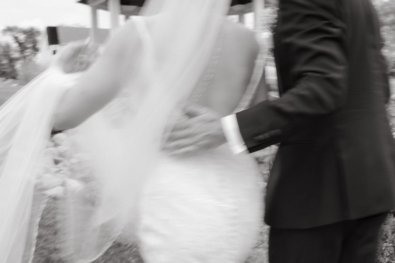 Blurred black and white artistic shot of bride in flowing veil walking with groom.