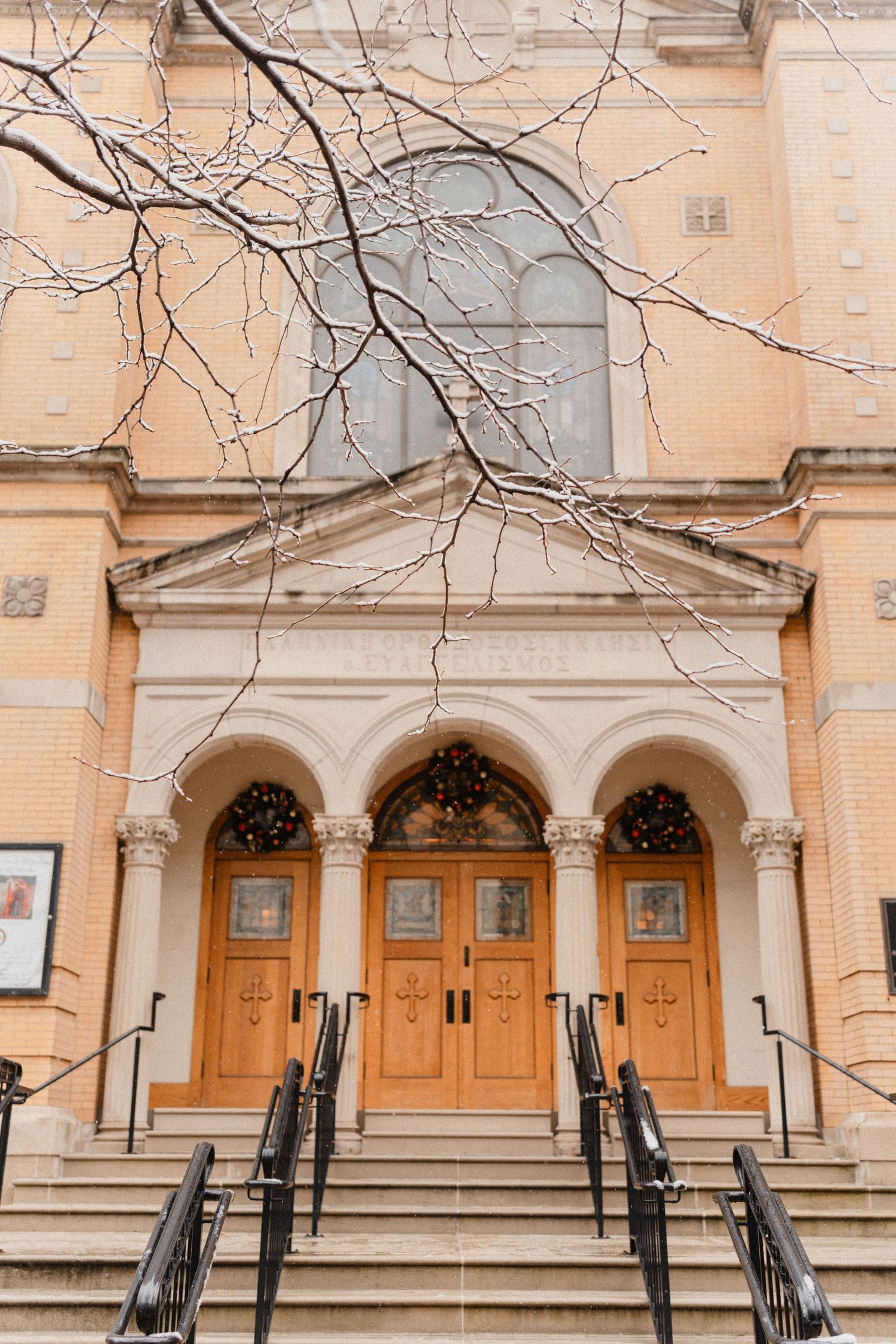 Elegant church exterior with wooden arched doors, stone steps, and bare winter branches framing the classical facade.