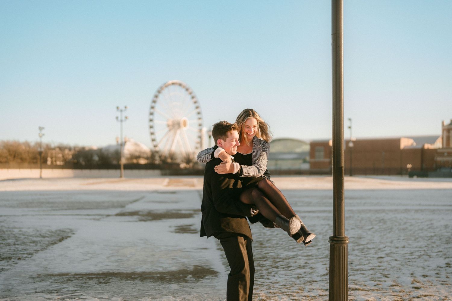 Man lifting woman near Ferris wheel in snowy Chicago winter outdoor setting.