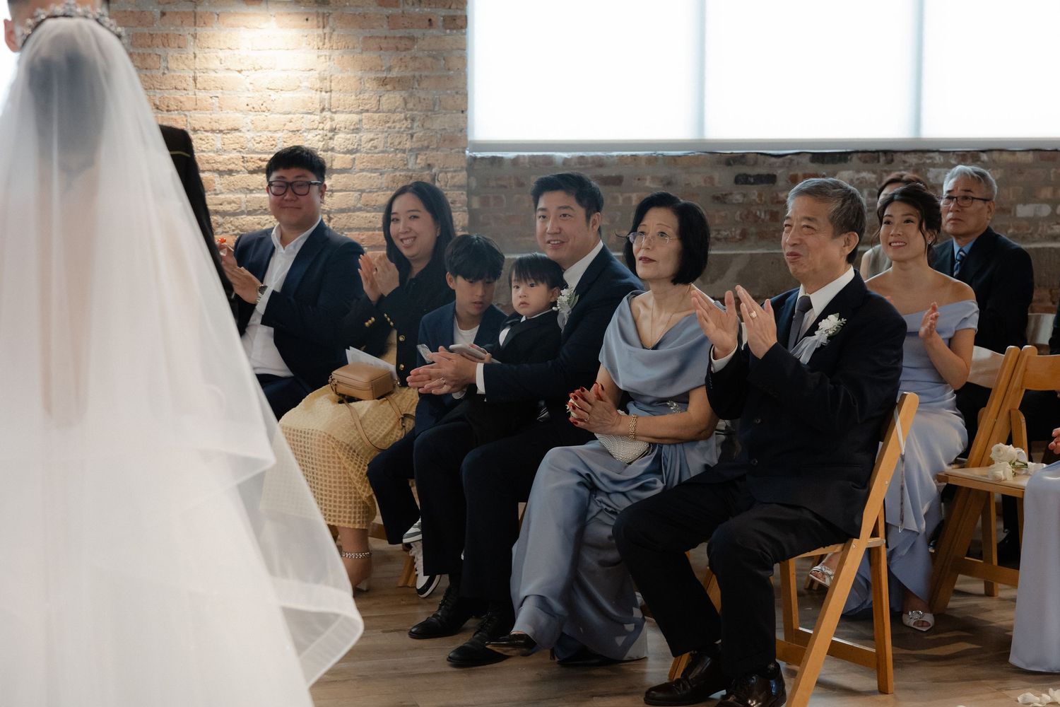 Wedding guests clapping and celebrating during an indoor ceremony with brick wall backdrop.