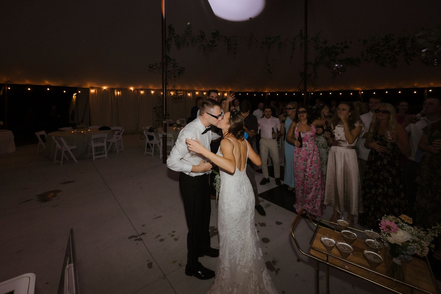 Bride and groom share a romantic first dance under string lights at their wedding reception.