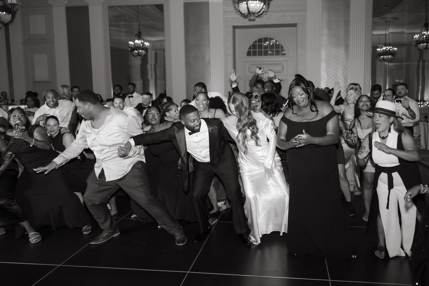 Black and white photo of wedding guests dancing energetically on the dance floor at a elegant wedding reception.