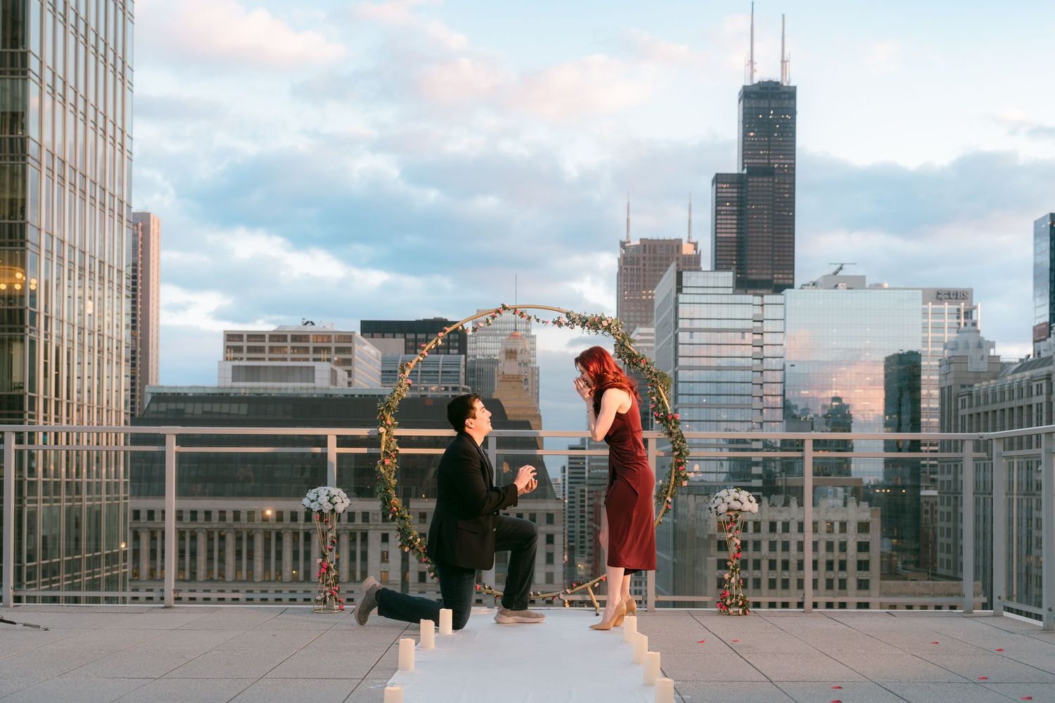 A romantic rooftop marriage proposal with a floral arch and the Chicago city skyline at sunset.