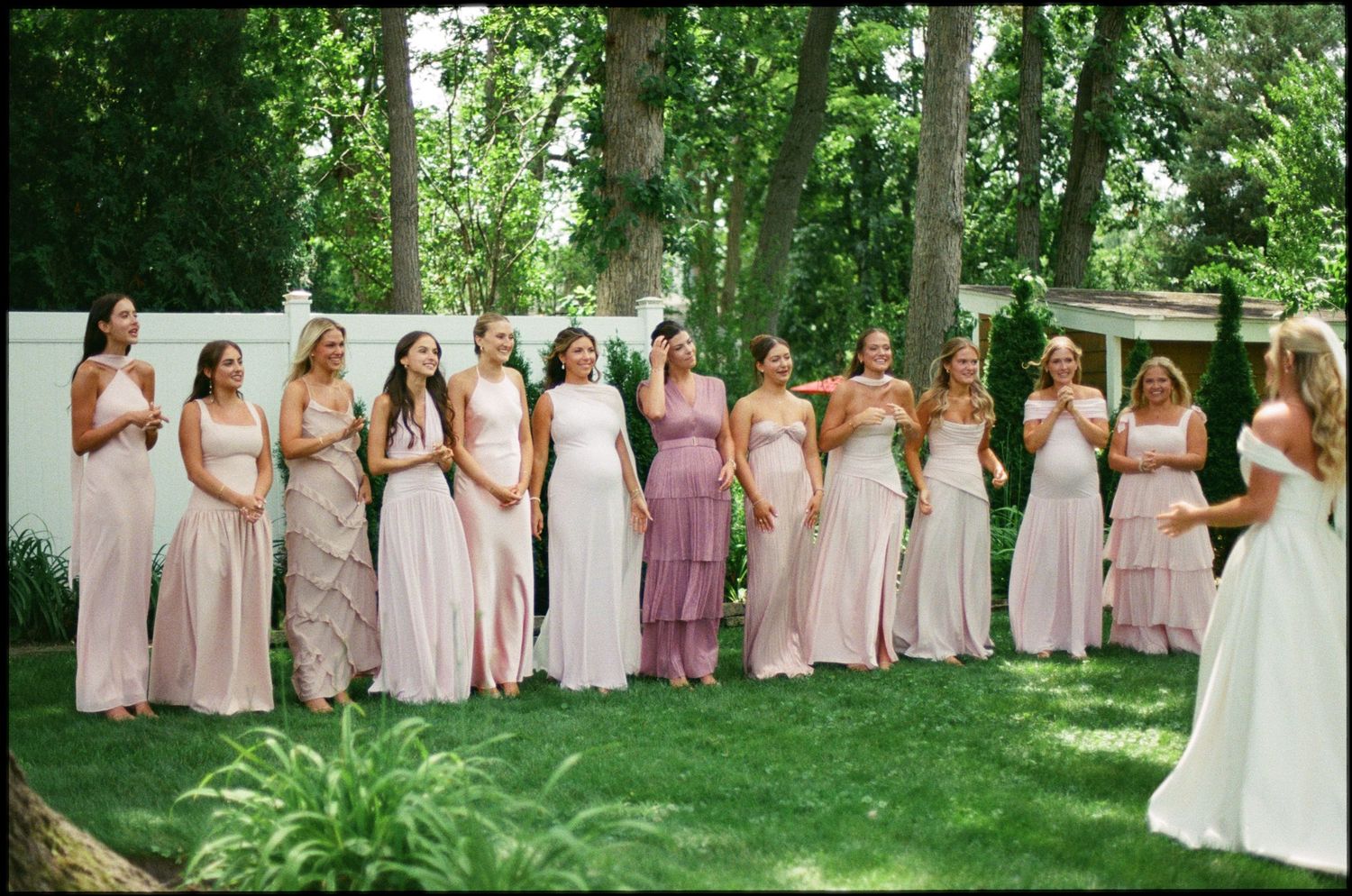 Group of bridesmaids in pink dresses standing outdoors at a garden wedding ceremony.