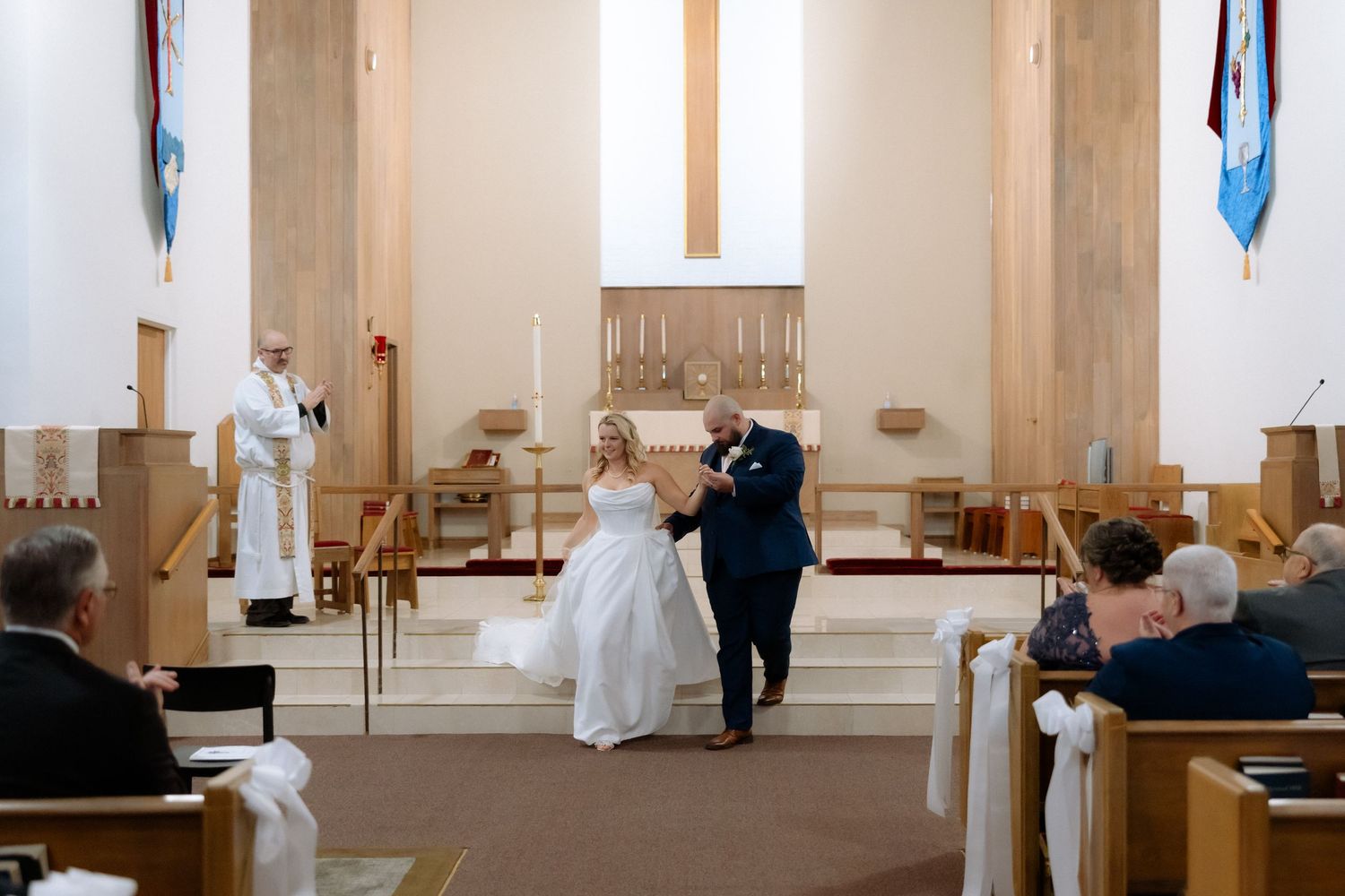 Bride and groom exchange vows at church altar during wedding ceremony with guests seated in wooden pews.