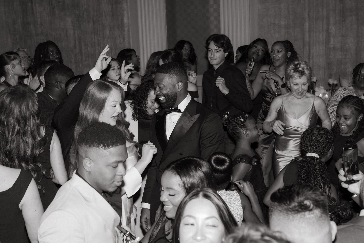 Black and white photo of elegantly dressed guests dancing and socializing at a formal event or gala.