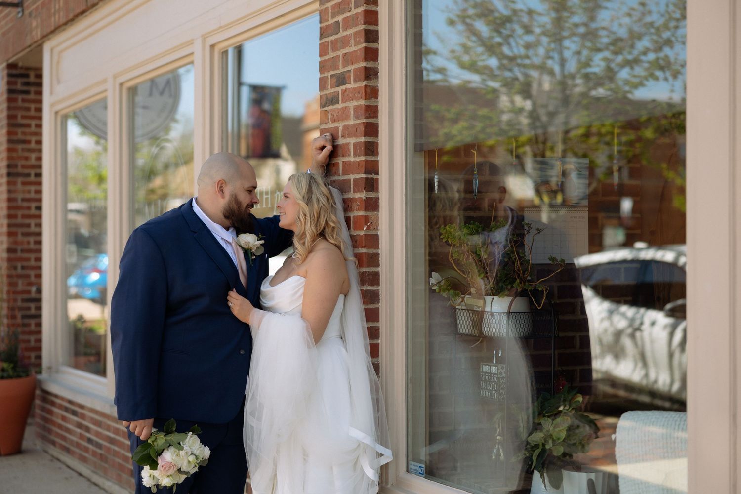 A bride and groom share a romantic moment outside a brick building, with the bride in a white gown and veil.