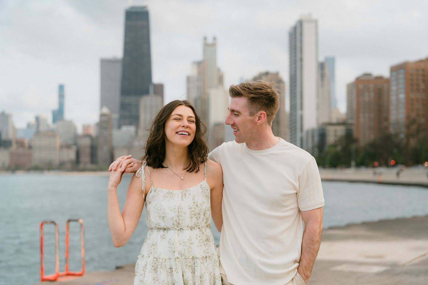 Laughing couple standing together on Chicago lakeside with cloudy city skyline backdrop.