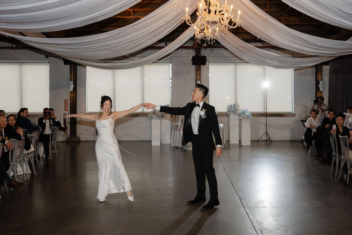 Bride and groom share their first dance in an elegant wedding venue with draped ceiling and chandelier.