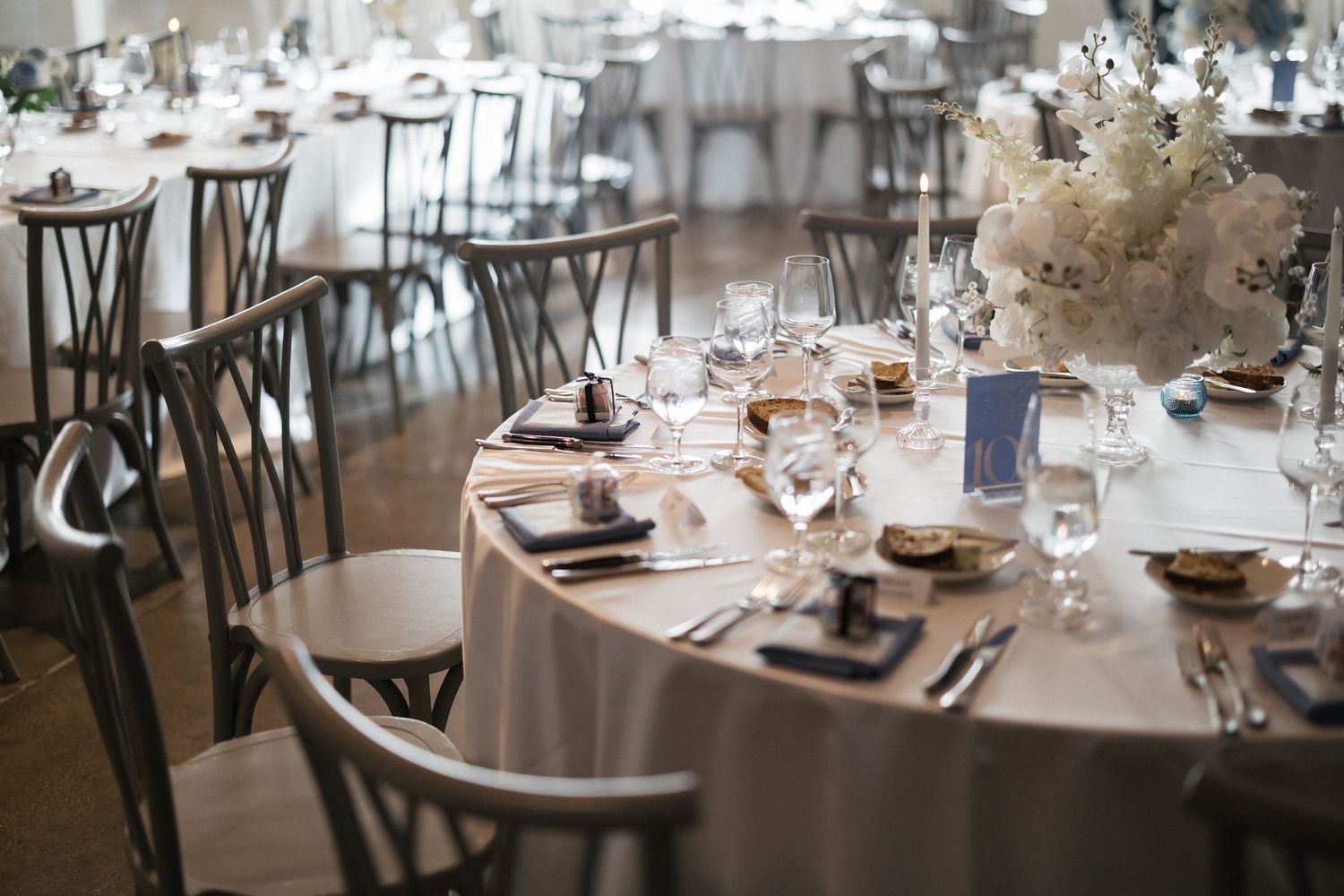 Elegant wedding reception table with white floral centerpiece, crystal glassware, and dark napkins on silver linens.