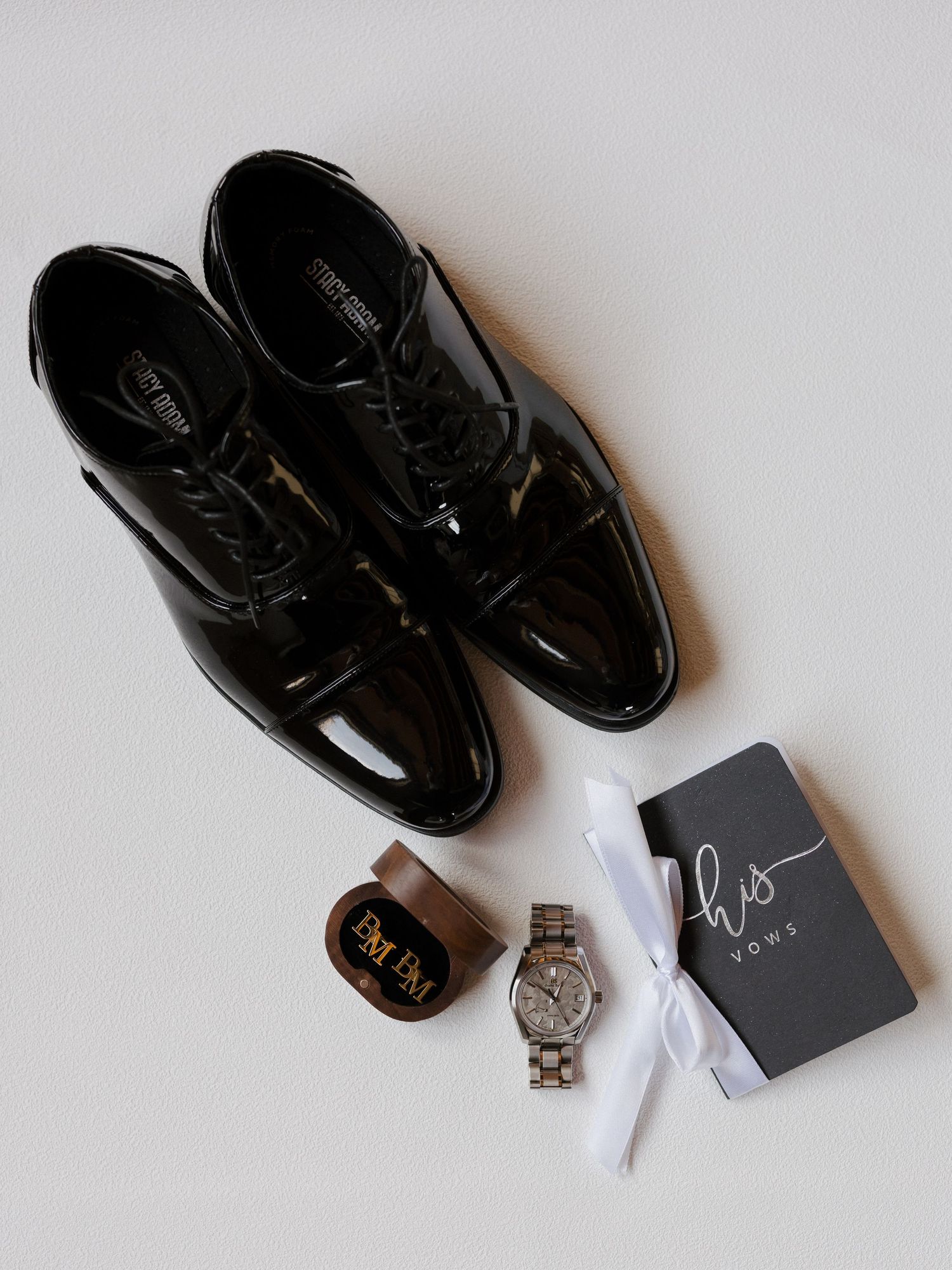 Groom wedding flat lay with black patent leather shoes, watch, monogram box, and his vows booklet.