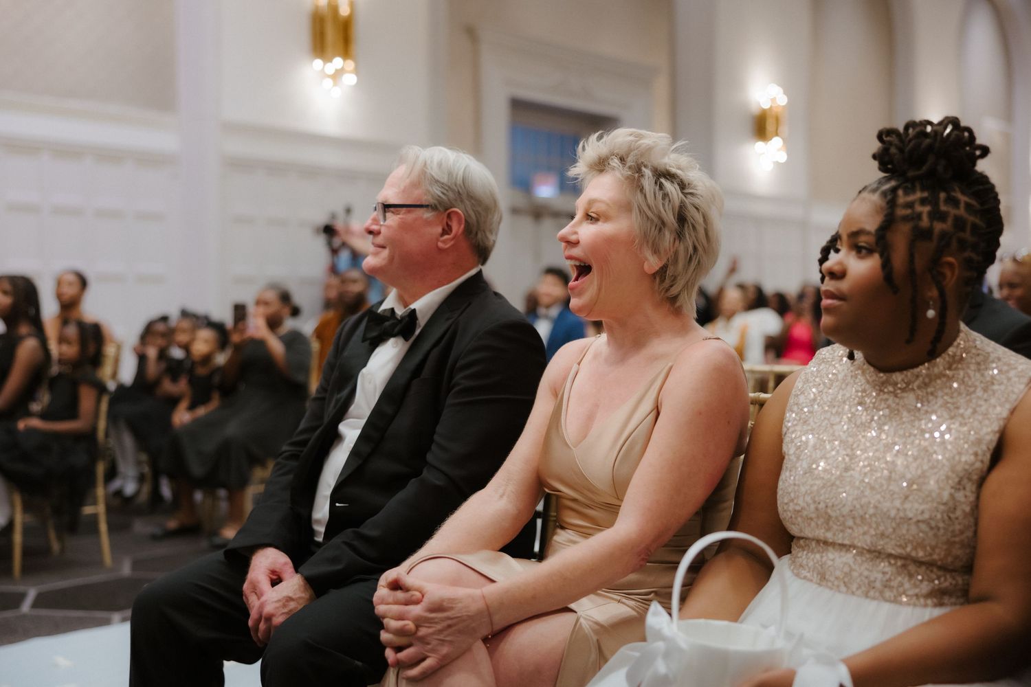 Guests laughing and smiling during a wedding ceremony in an elegant ballroom venue.