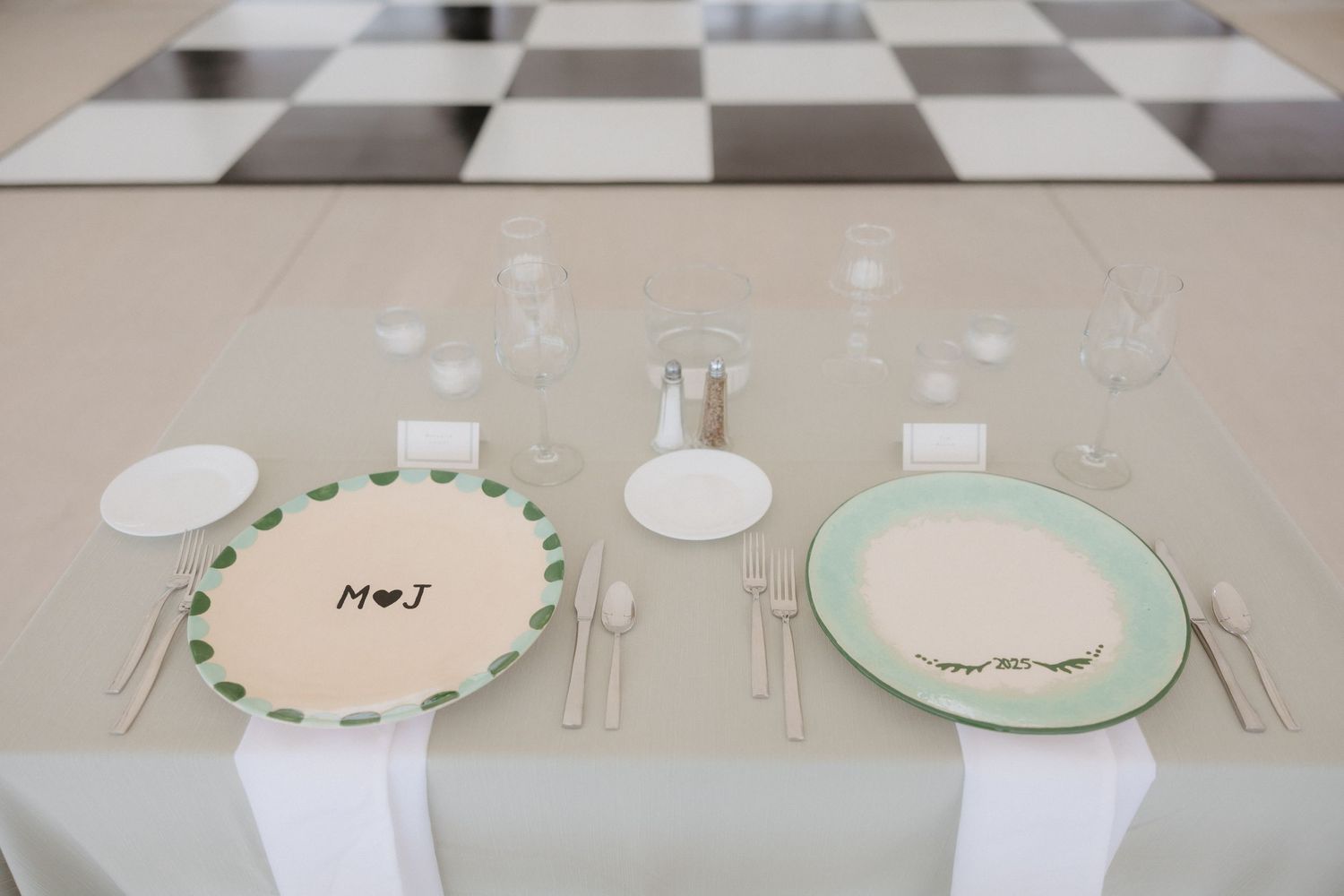 Wedding table setting with personalized plates monogrammed M+J, glassware, and white linen runner.