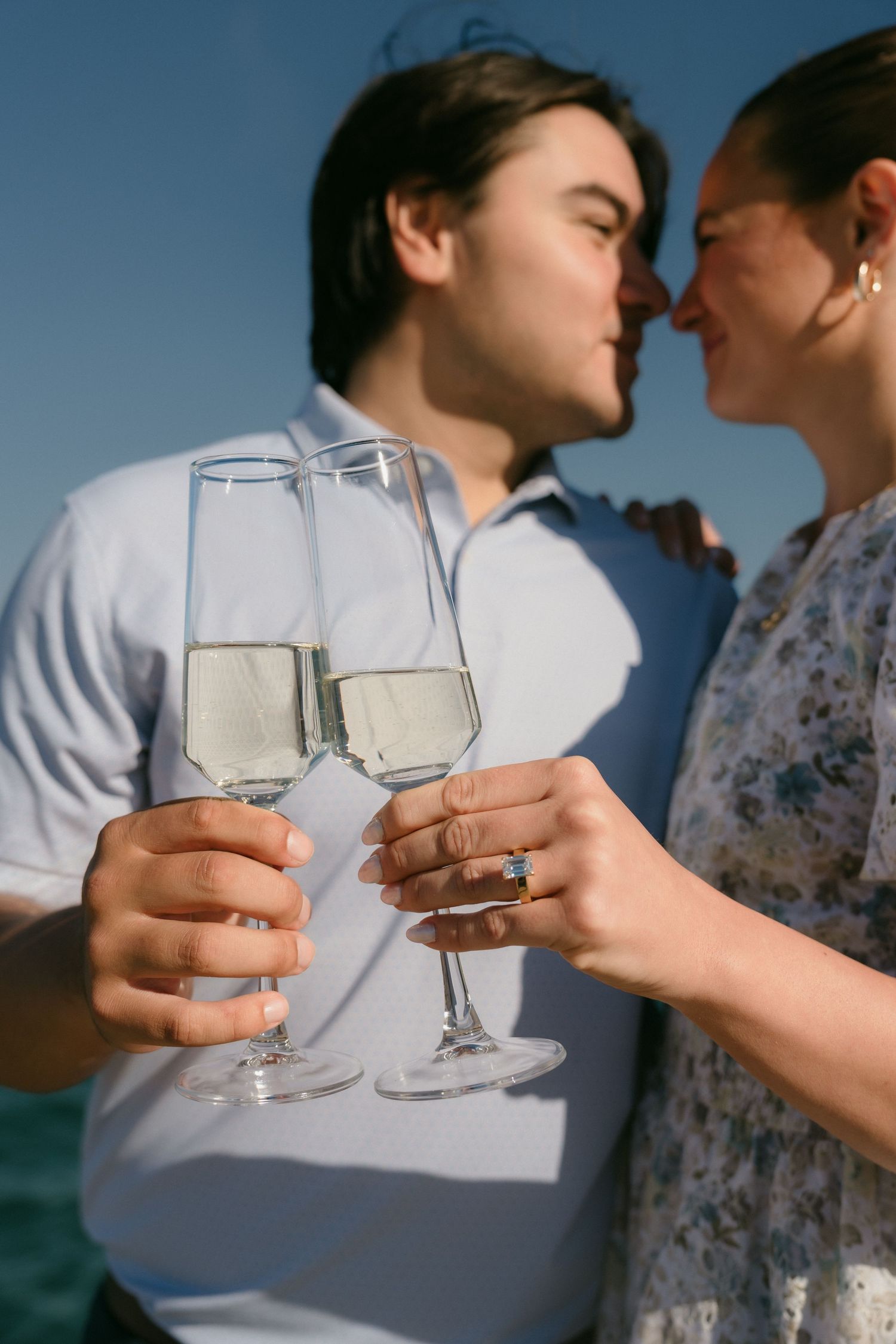 Close-up of engaged couple clinking champagne glasses with engagement ring visible on hand.