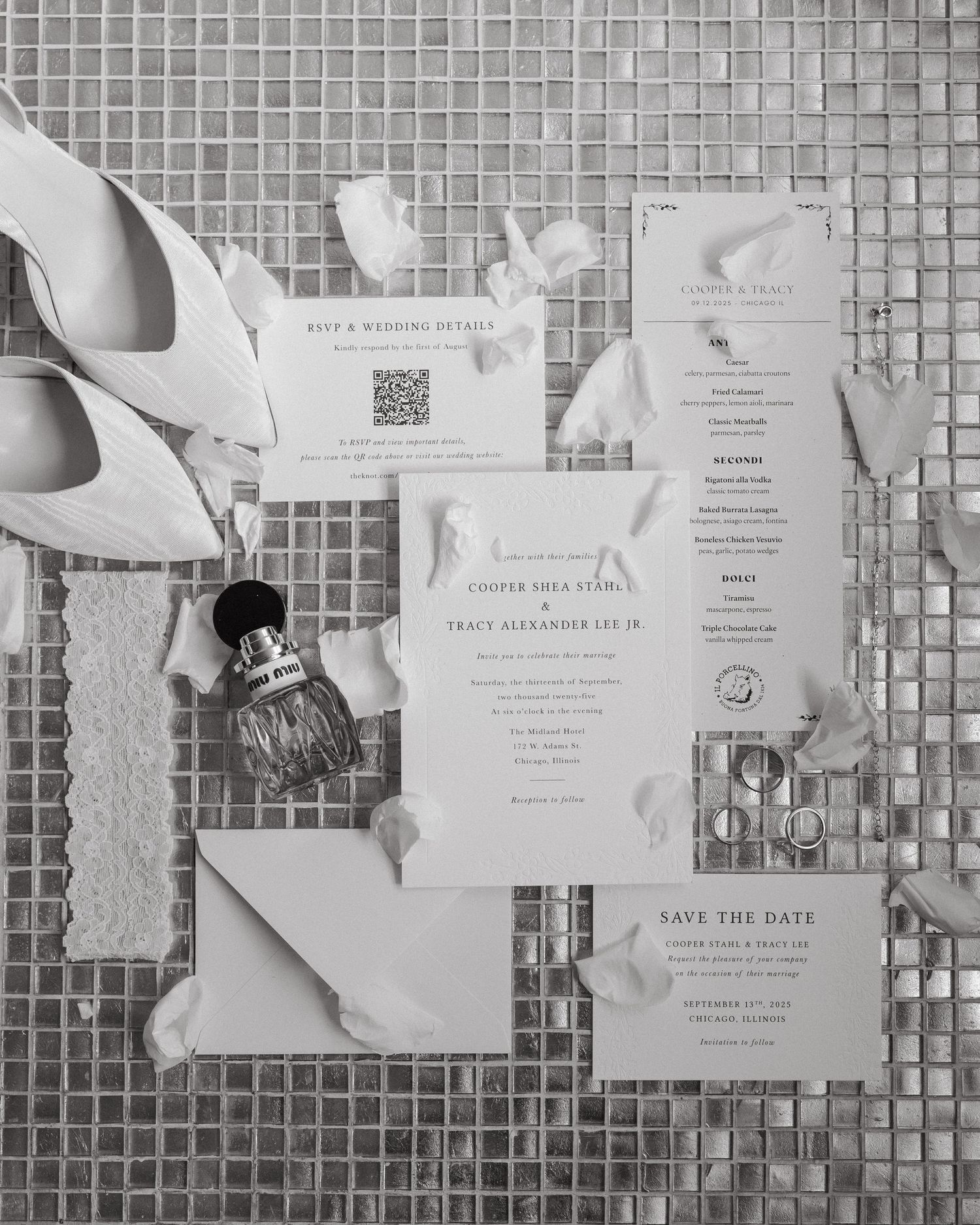 Black and white wedding flat lay with invitation suite, save the date, heels, perfume, and floral accents on mosaic tile.