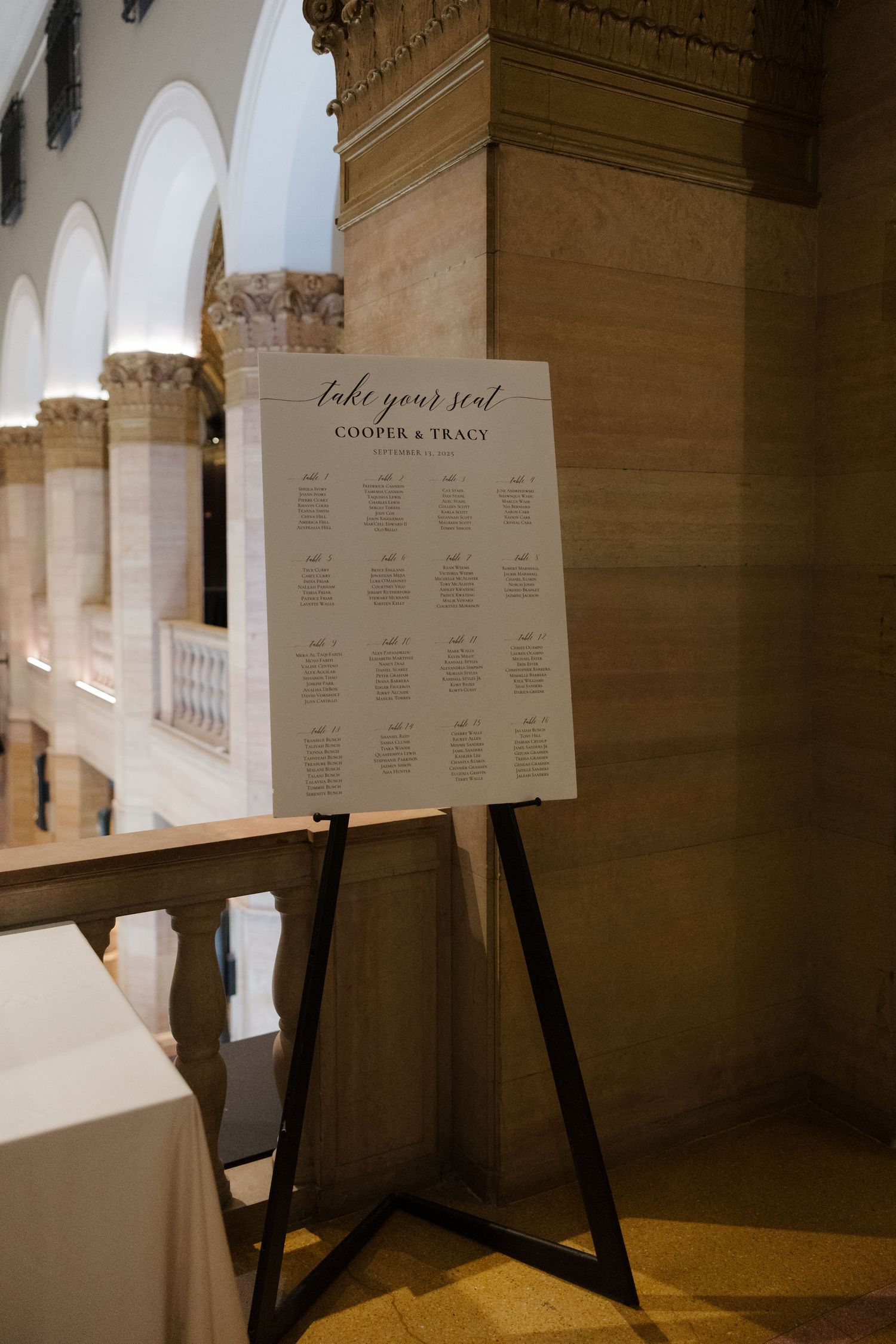 Elegant wedding seating chart on easel displaying Cooper & Tracy guest arrangements in a grand venue.