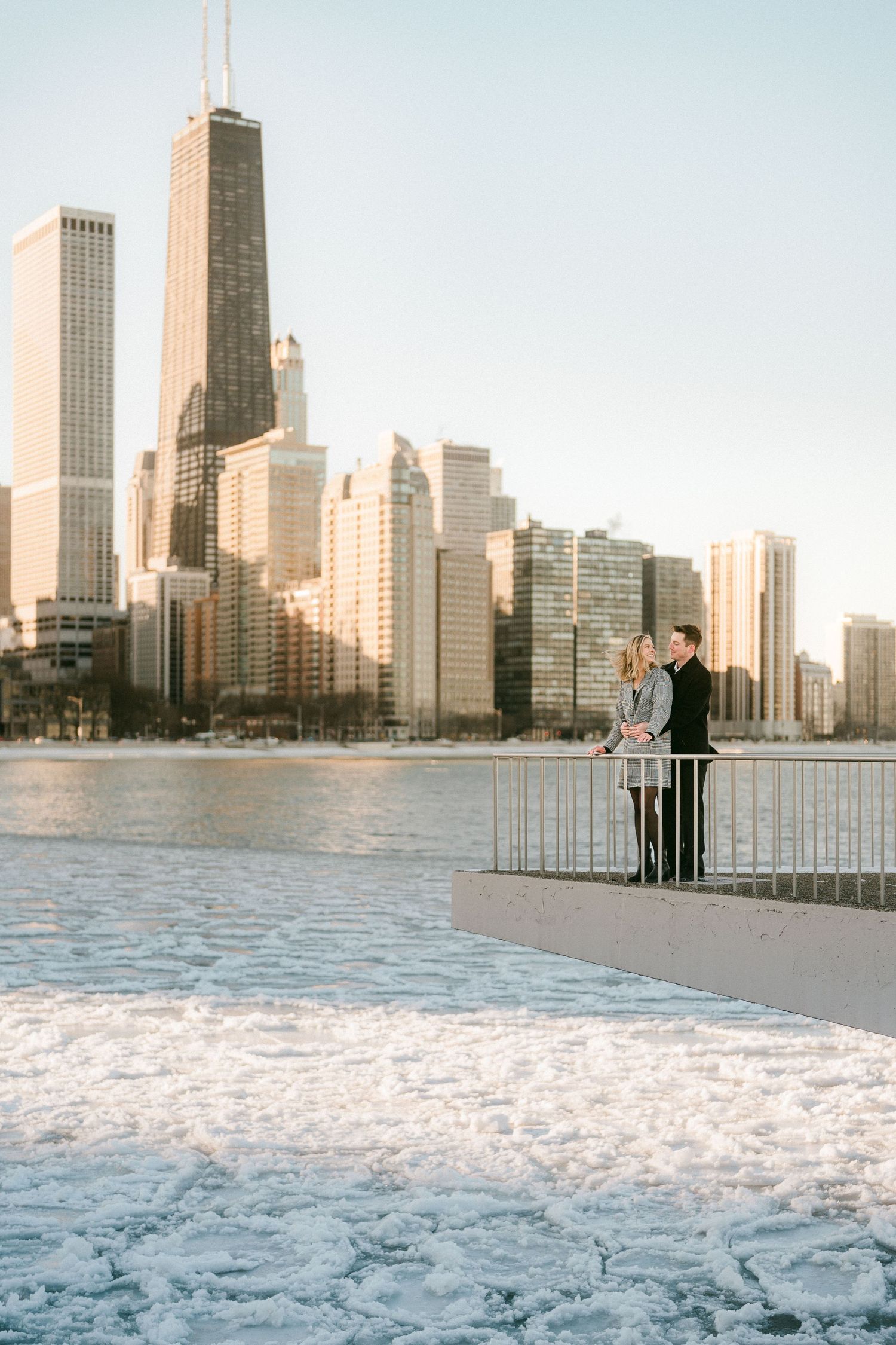 Couple standing at railing overlooking frozen Lake Michigan with Chicago skyline.