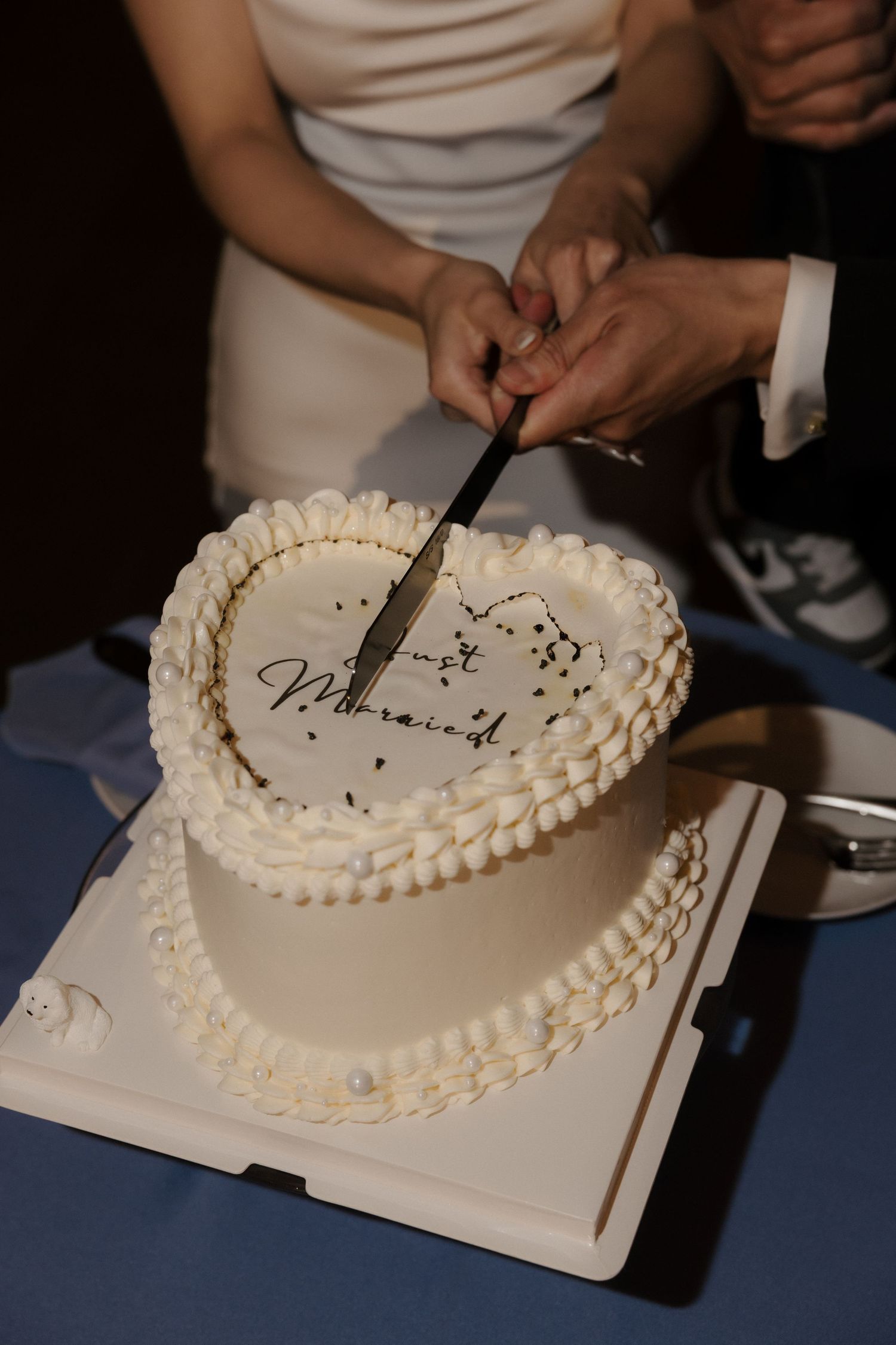 Bride and groom cutting a heart-shaped white wedding cake decorated with Just Married inscription.