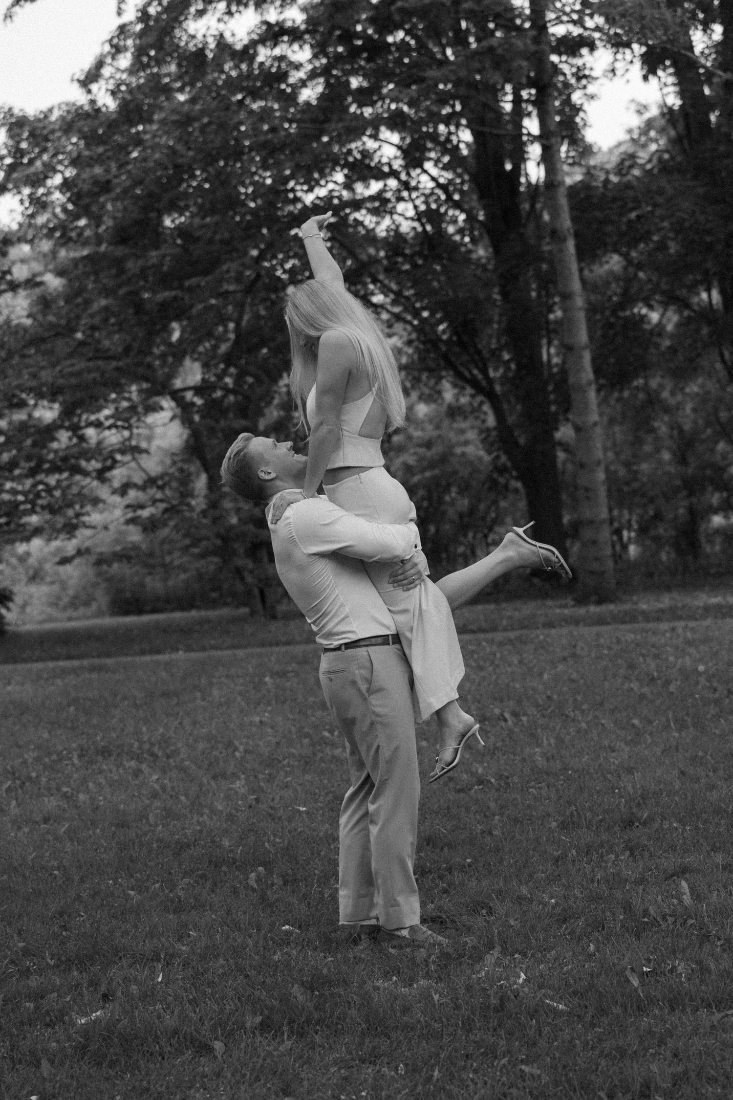 Black and white photo of man lifting woman high in air during romantic outdoor couples photography session.
