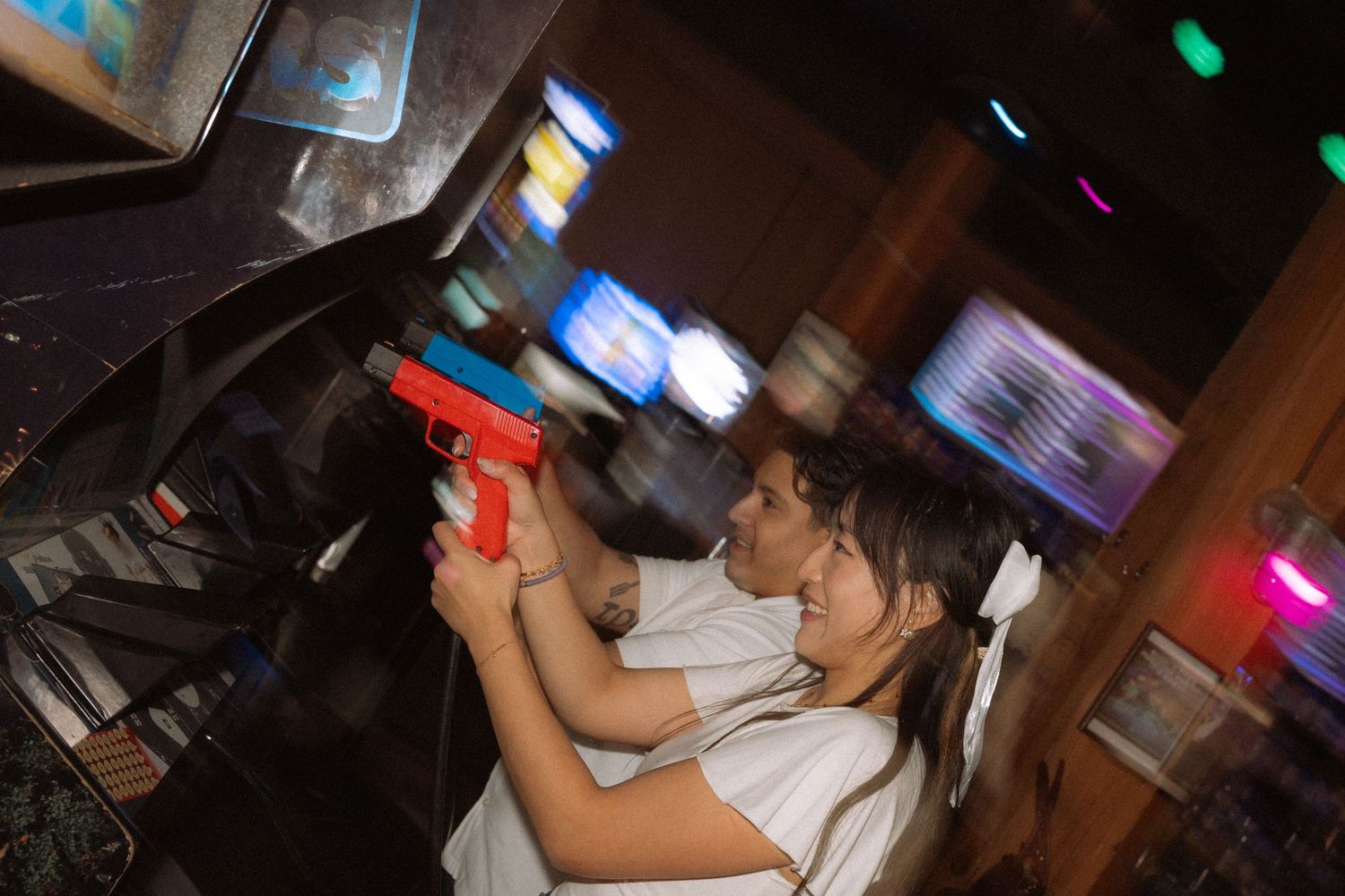 Woman aiming a red toy gun at an arcade shooting game in a dimly lit game room.