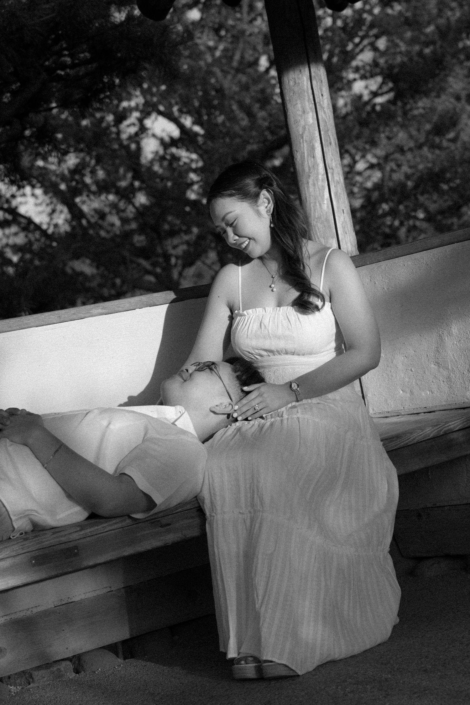 Black and white photo of two women relaxing on a bench outdoors, one lying down smiling up at the other.