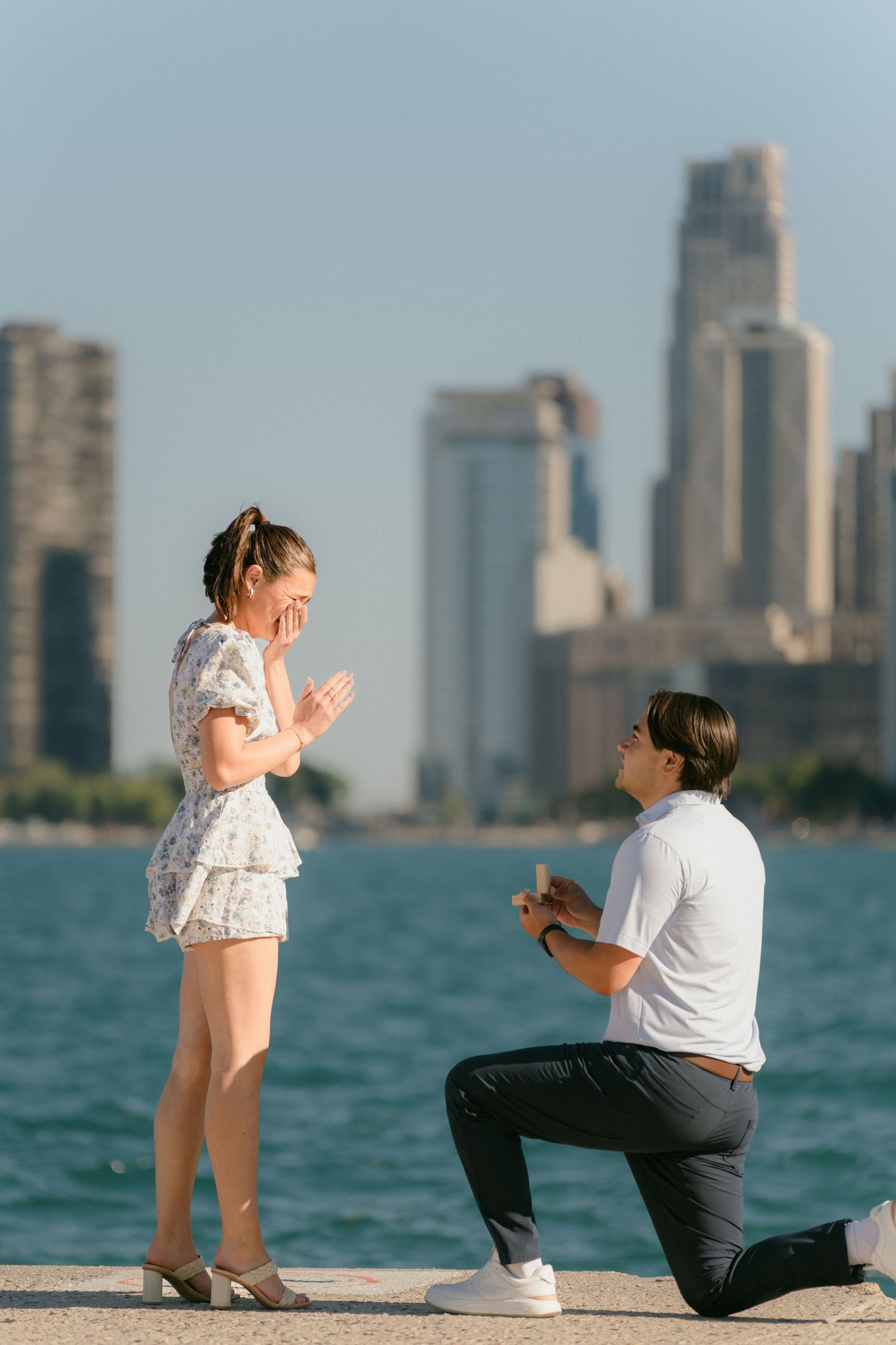 Man proposes to surprised woman on one knee by Chicago lakefront.