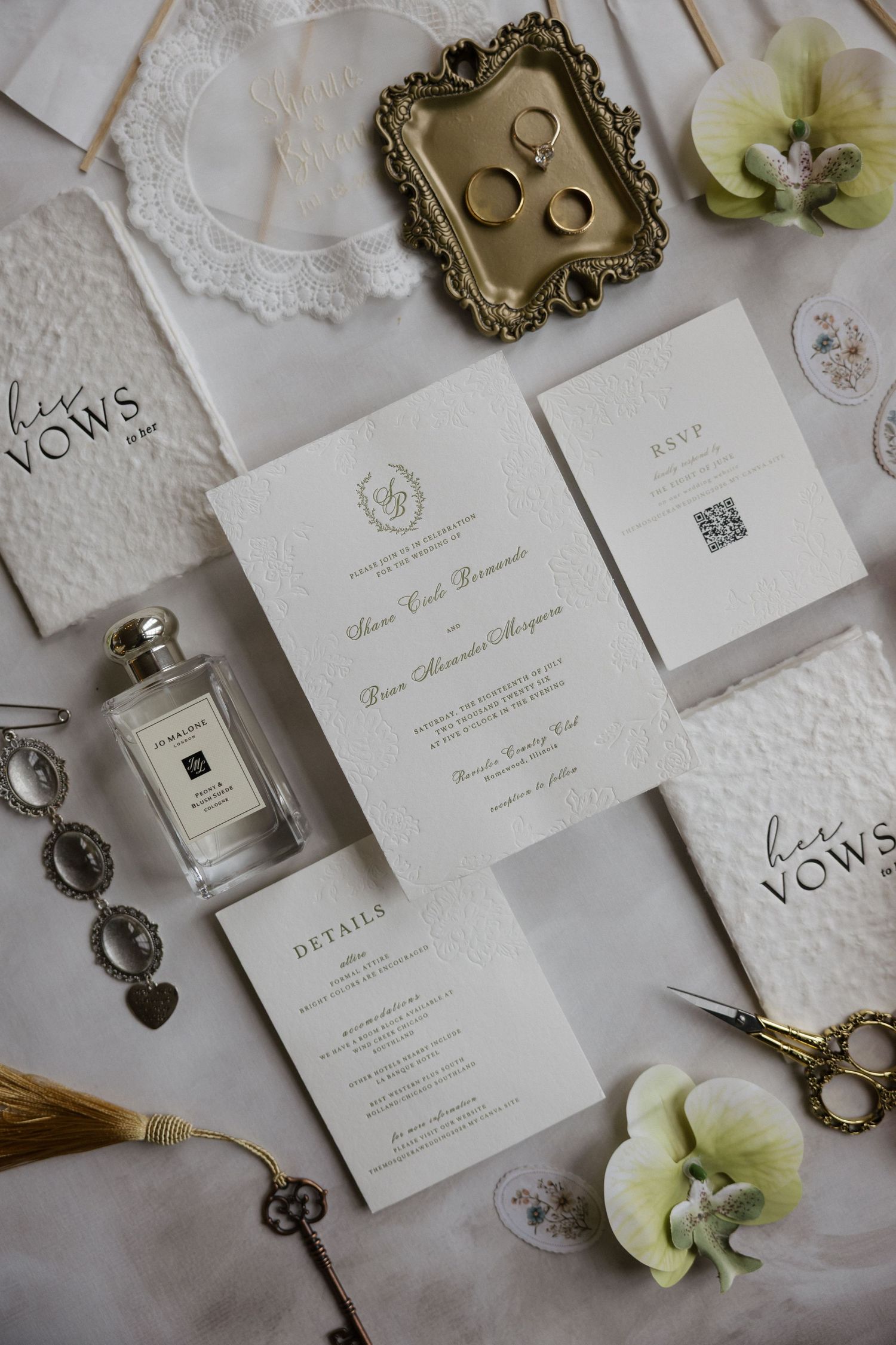 Elegant wedding stationery flat lay with gold rings, Jo Malone perfume, orchids, vow books, and scissors.
